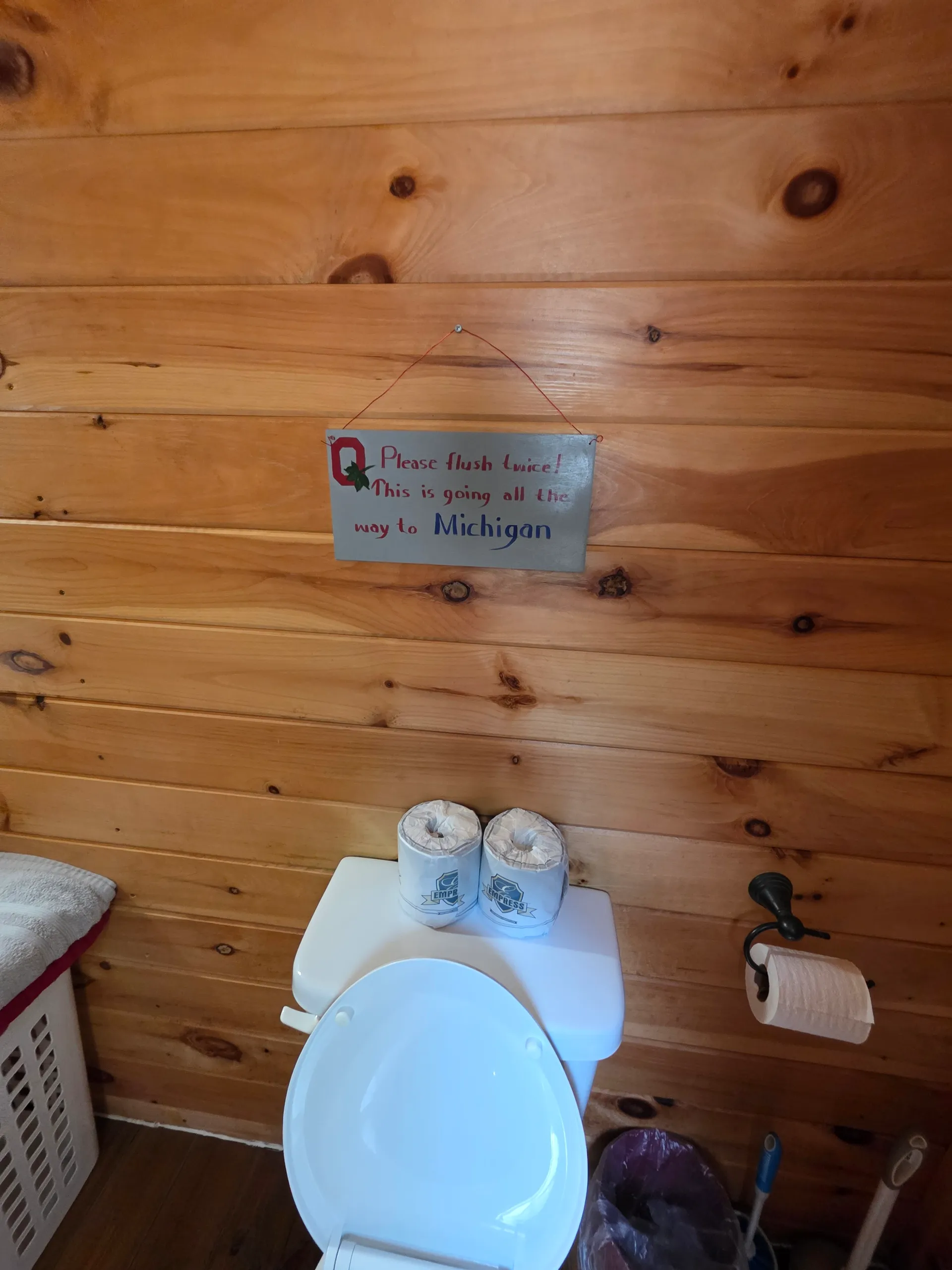 Bathroom with Ohio humor sign and pine-paneled walls at Buckeye Hut cabin
