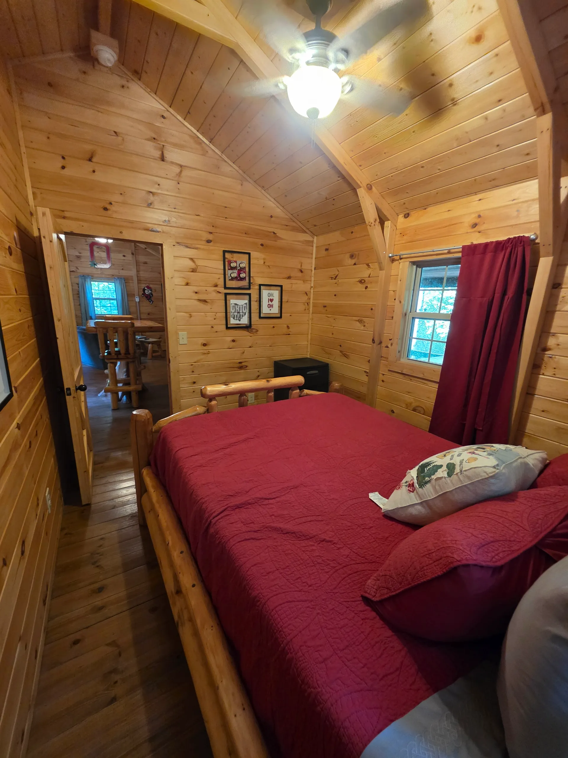 Loft bedroom overlooking living room below with red bedding and log bed frame at Buckeye Hut cabin