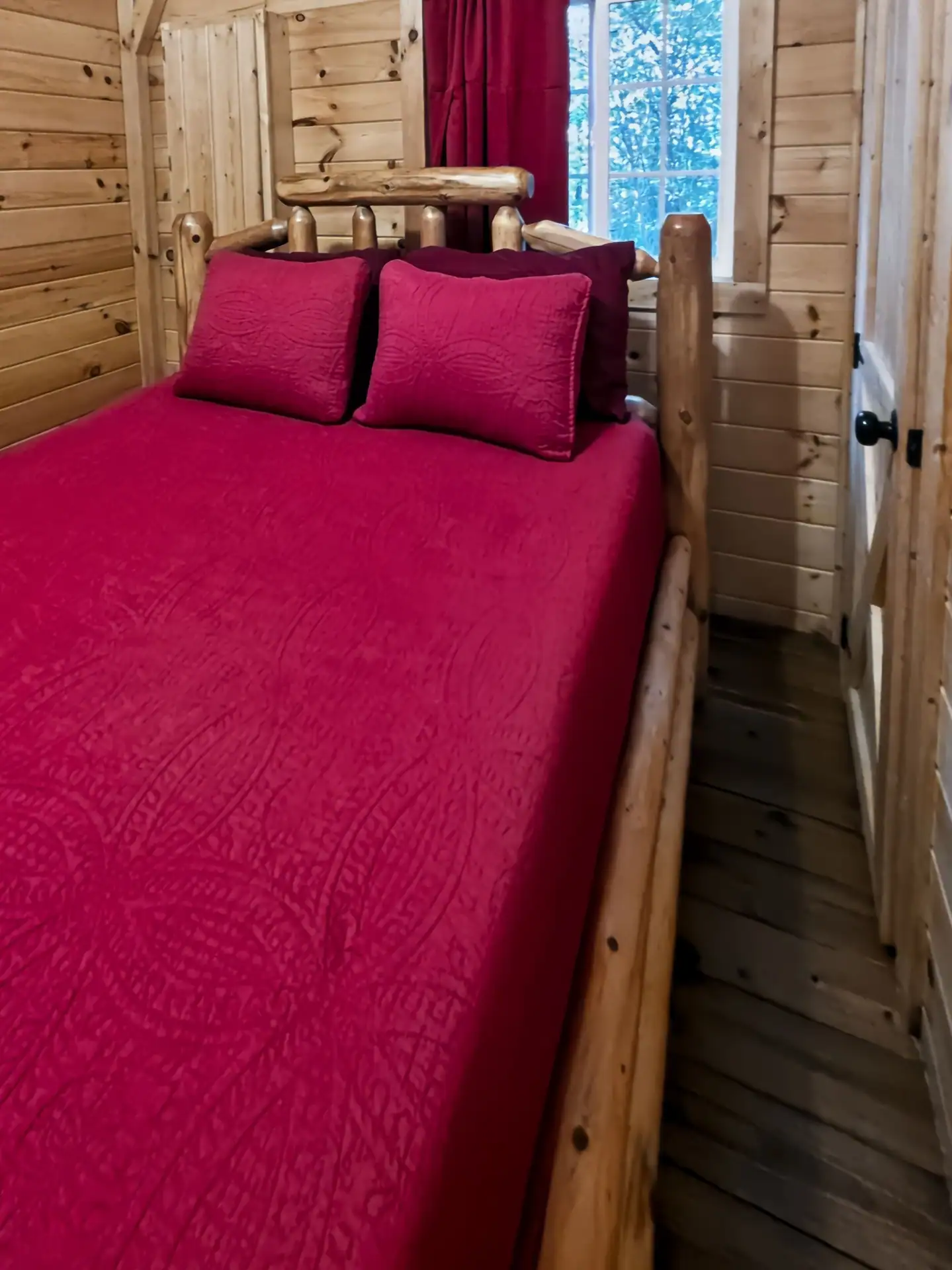 Bedroom with red bedspread and rustic log bed frame at Buckeye Hut cabin