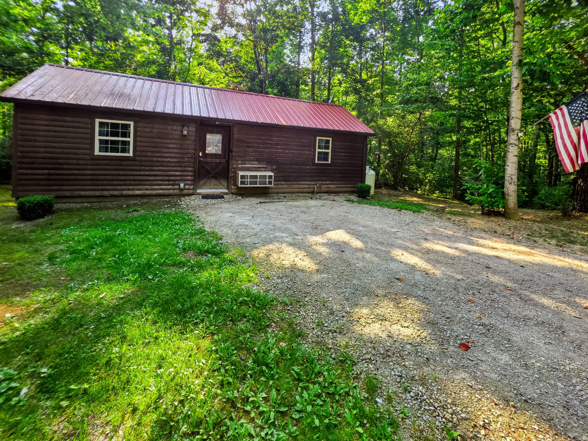 Buckeye Hut cabin seen from the lawn with gravel driveway and American flag