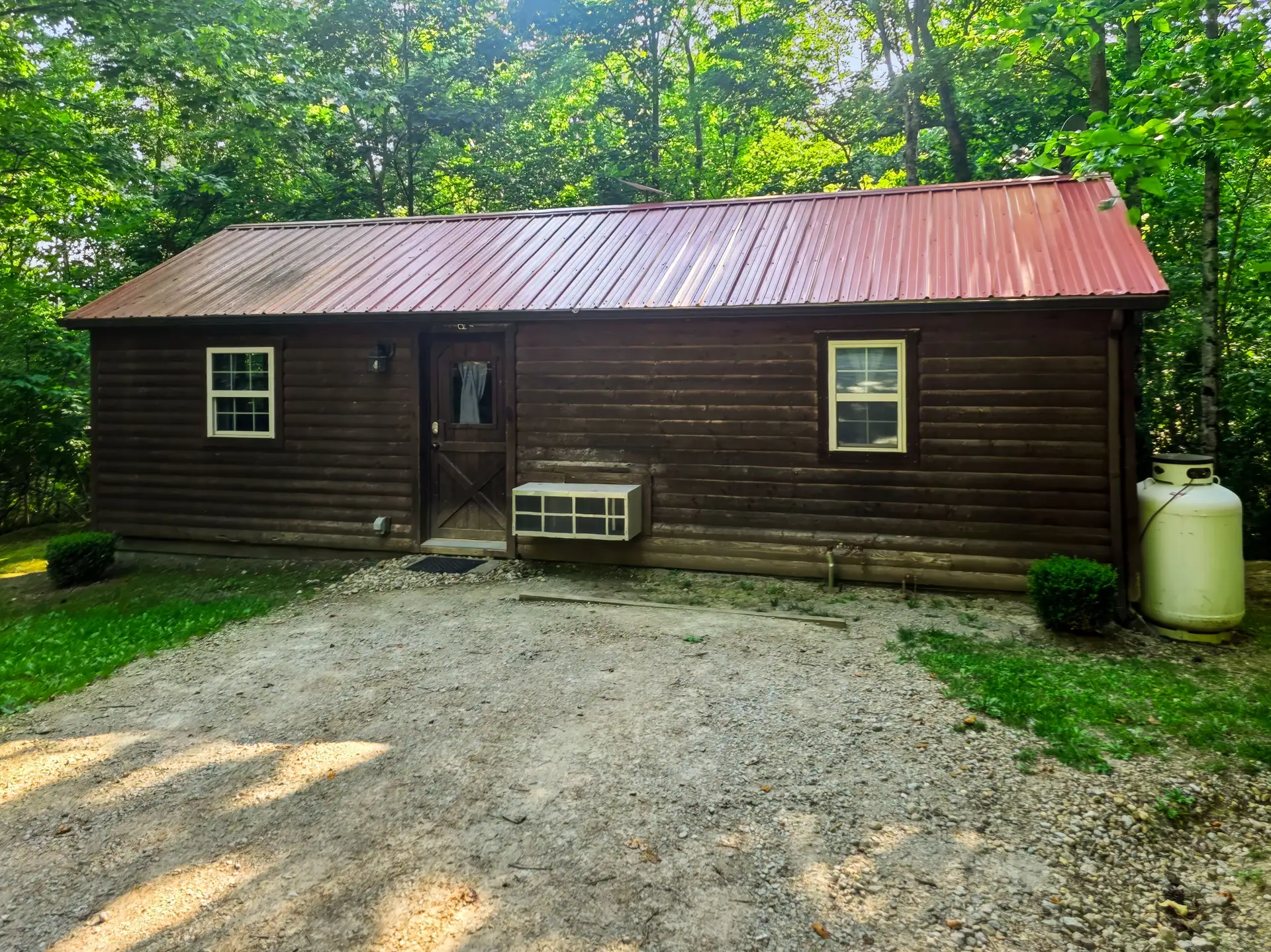 Front of Buckeye Hut log cabin with red metal roof and gravel parking area