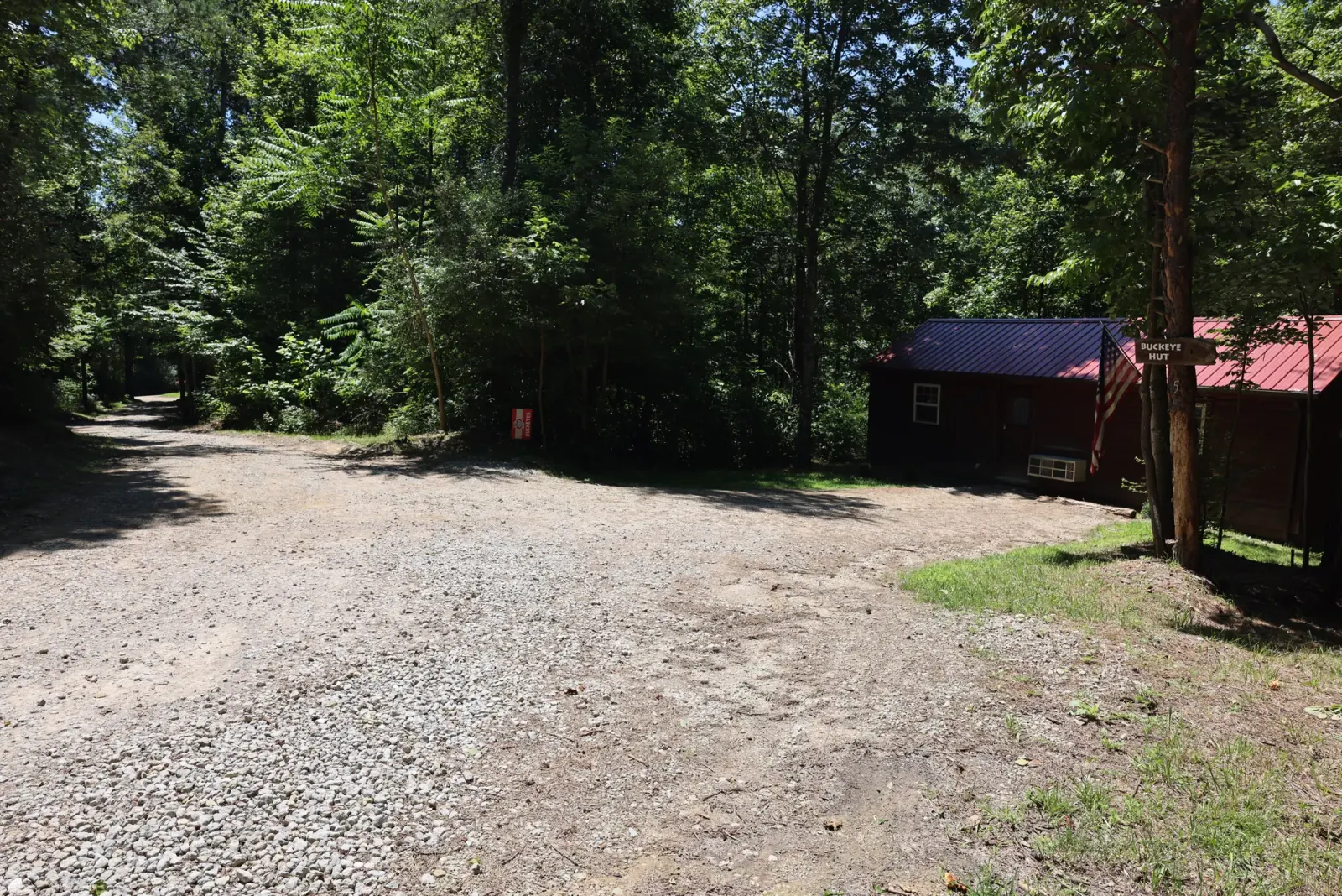 Gravel parking area with Buckeye Hut and neighboring cabin visible among the trees