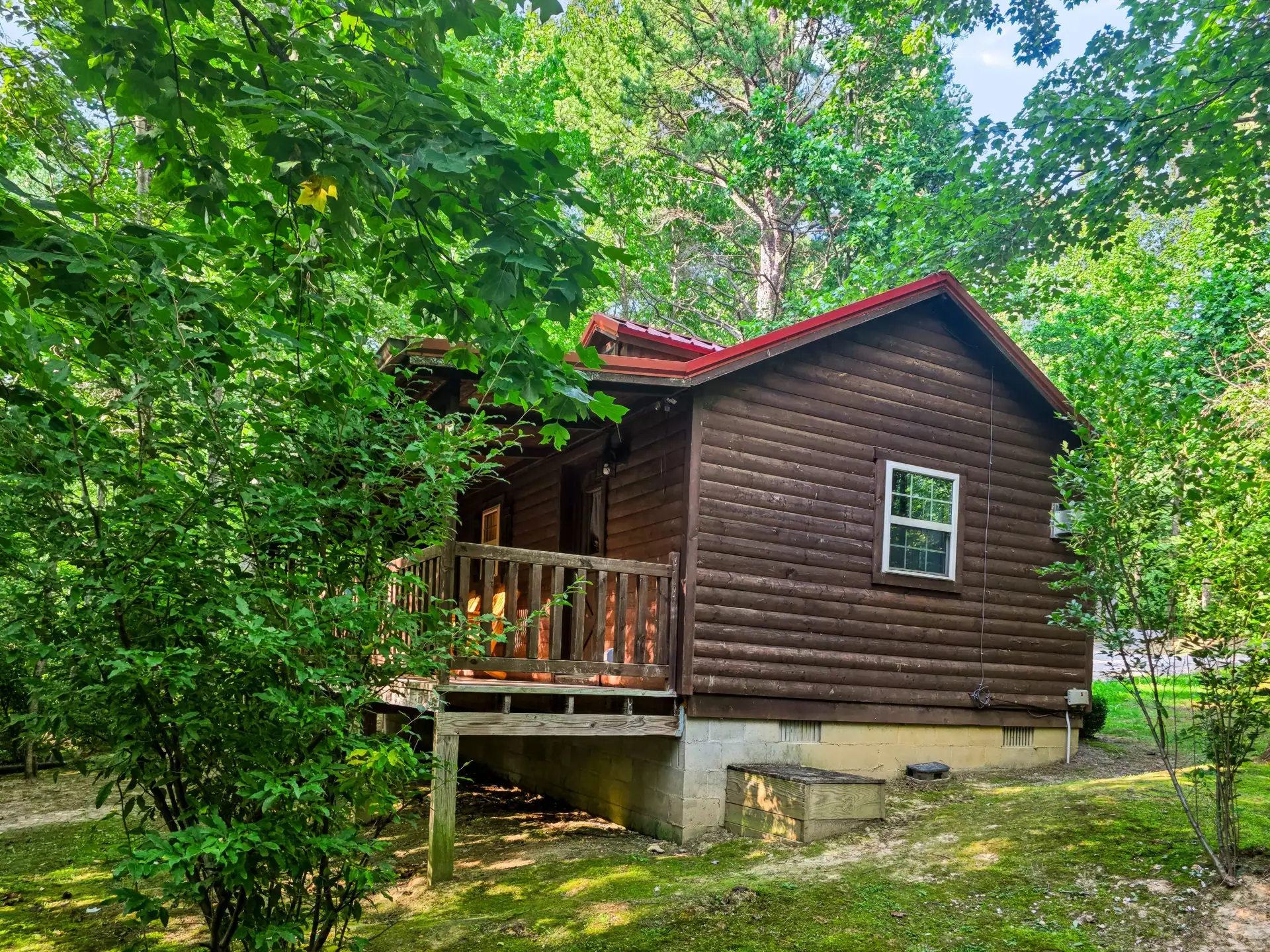 Side of Buckeye Hut cabin with porch railing surrounded by green trees