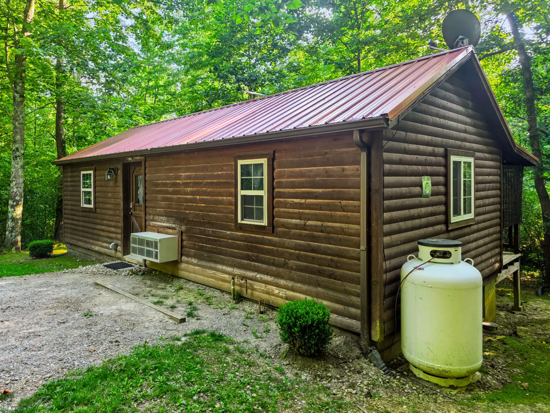 Side view of Buckeye Hut log cabin with red metal roof set in the woods