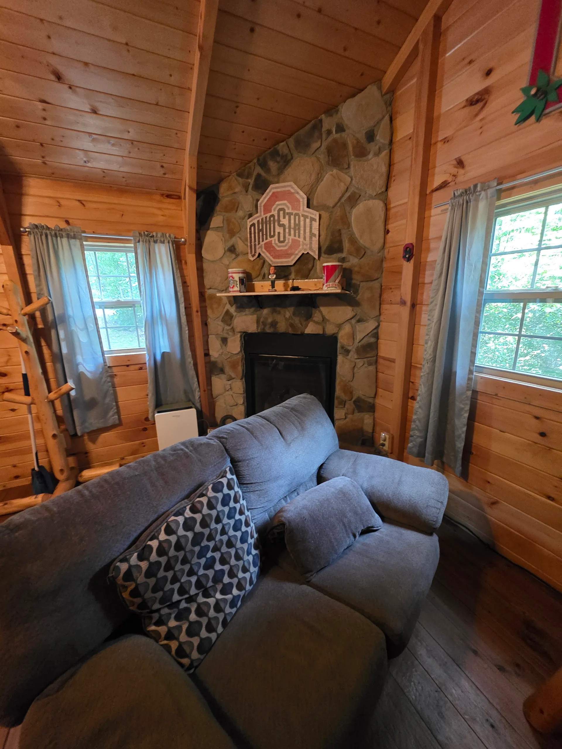 Stone fireplace with gray sofa and Ohio State themed decor in the living room at Buckeye Hut cabin