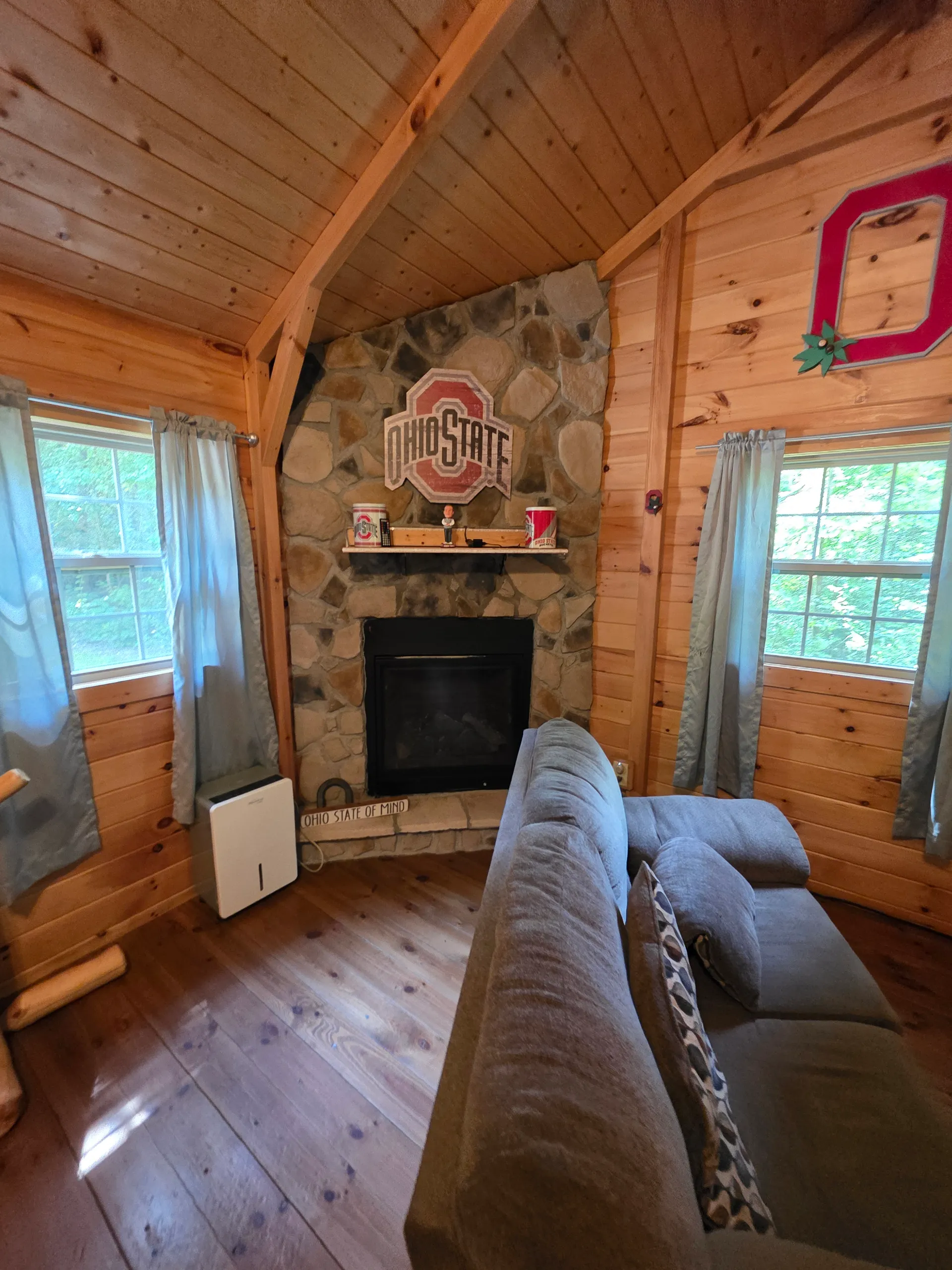 Stone fireplace with Ohio State decor and gray sofa in the pine-paneled living room at Buckeye Hut cabin