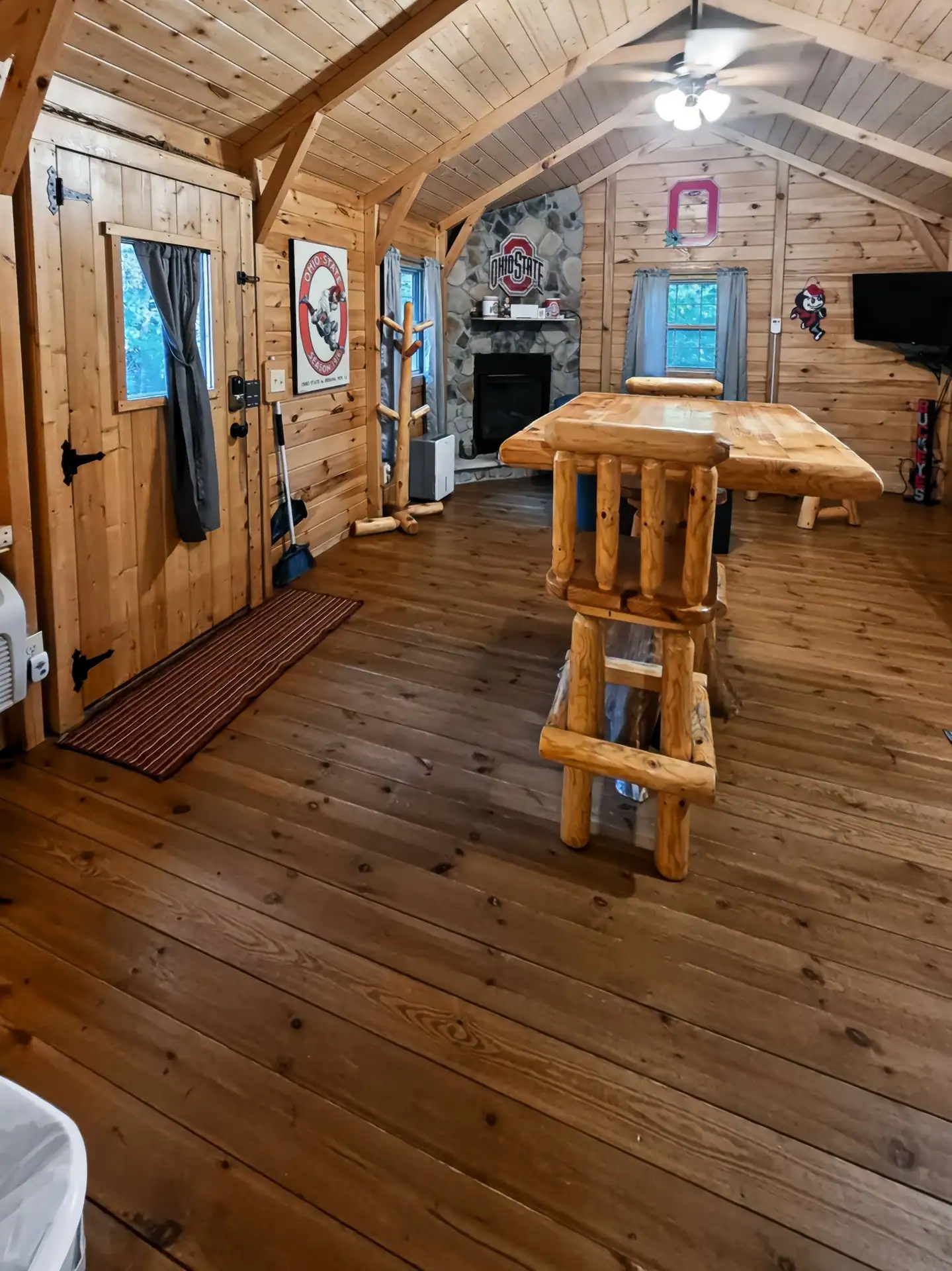 Open living area at Buckeye Hut cabin with pine walls, vaulted ceiling, log table, and stone fireplace