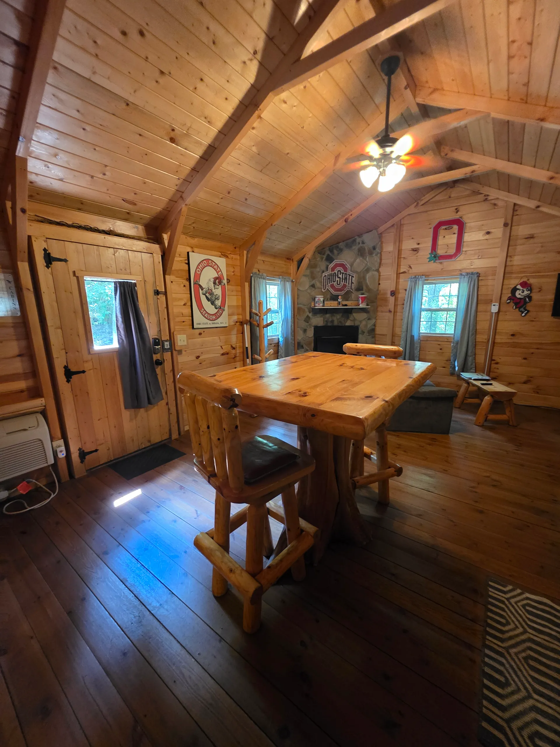 Wide view of pine-paneled living room with log furniture, stone fireplace, and vaulted A-frame ceiling at Buckeye Hut cabin