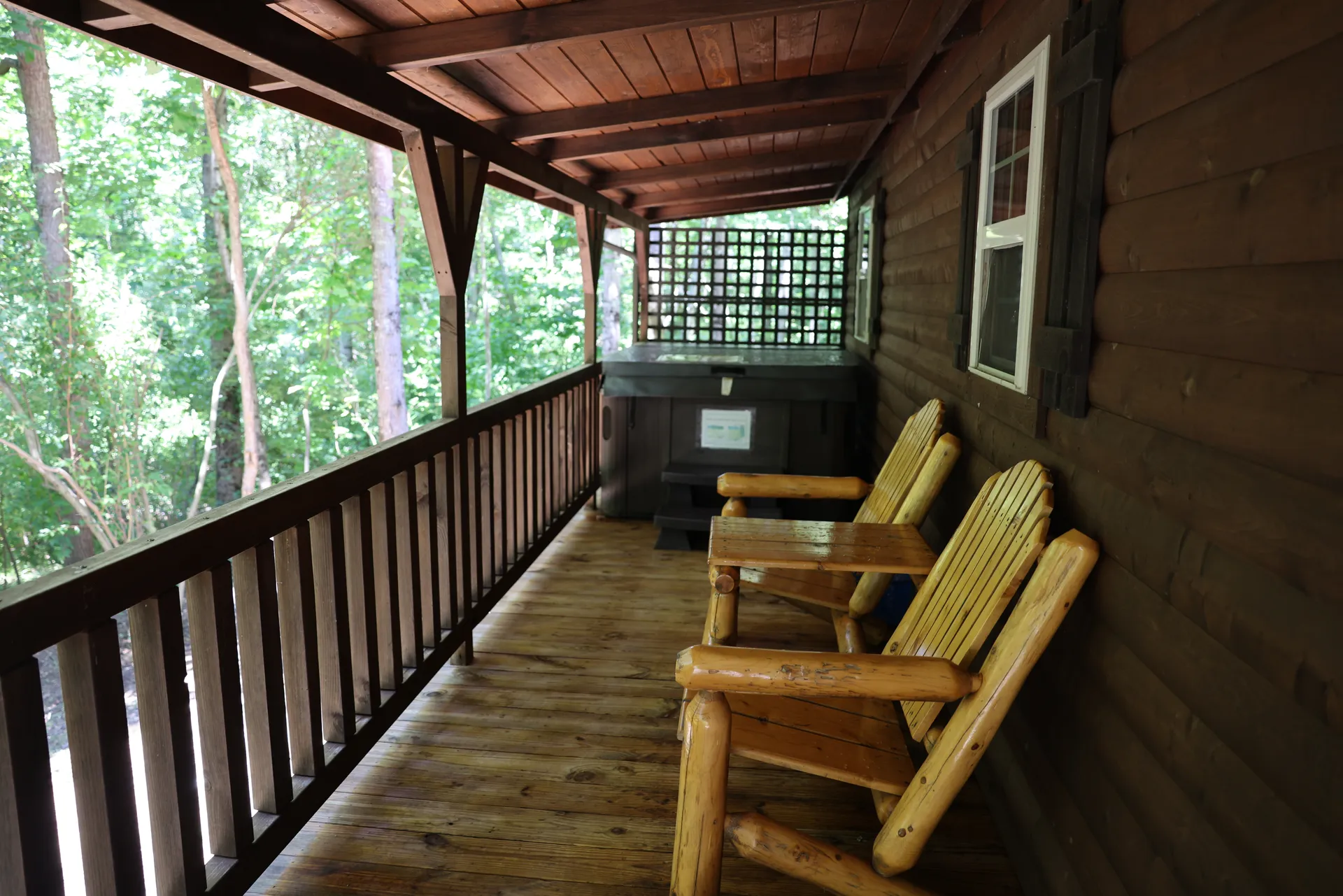 Covered porch with hot tub and log Adirondack chairs overlooking the forest at Buckeye Hut cabin