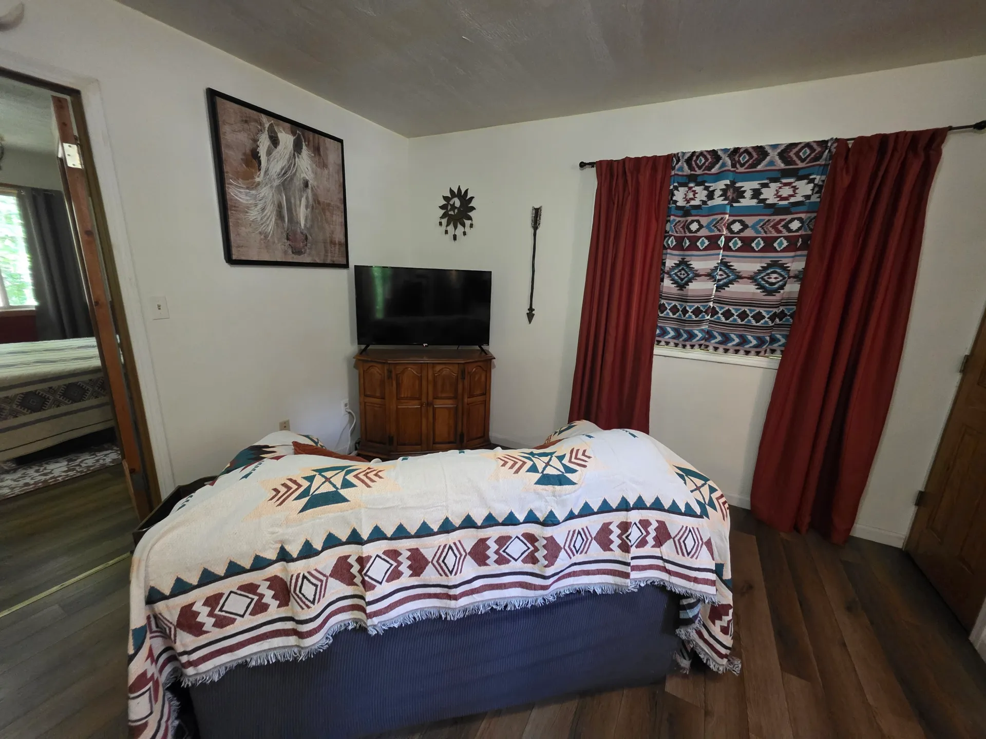 Bedroom with queen bed, Southwestern blanket, wall-mounted TV, and patterned tapestry at Cherokee Way cabin