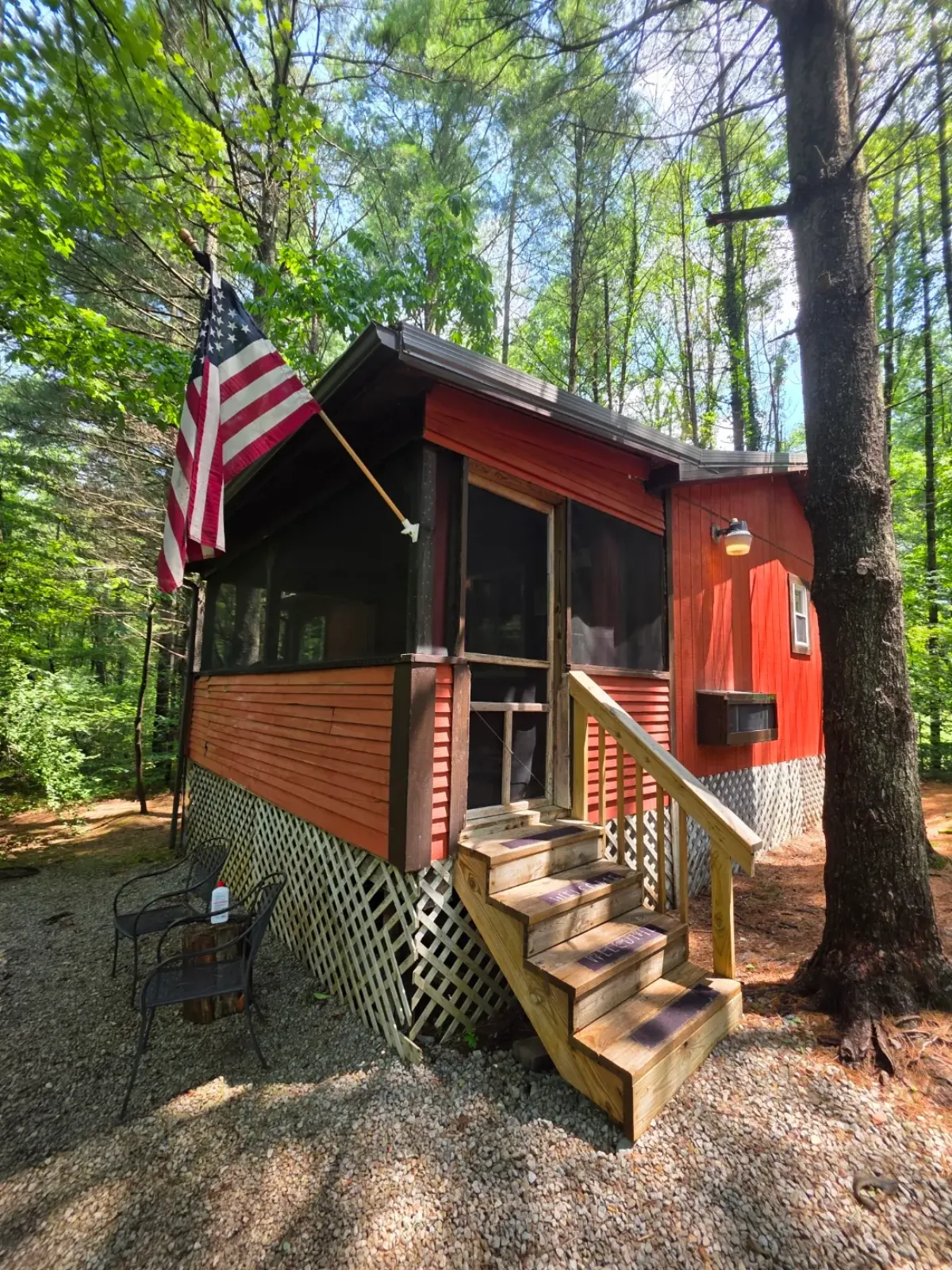 Red cabin with upper deck, stairs, and lattice skirting in the wooded setting at Cherokee Way