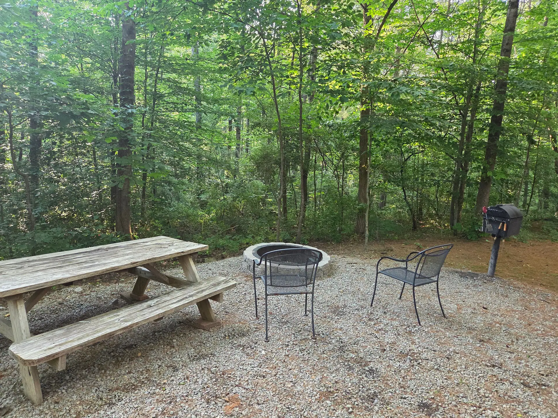 Stone fire pit with chairs, picnic table and charcoal grill in the woods at Cherokee Way cabin