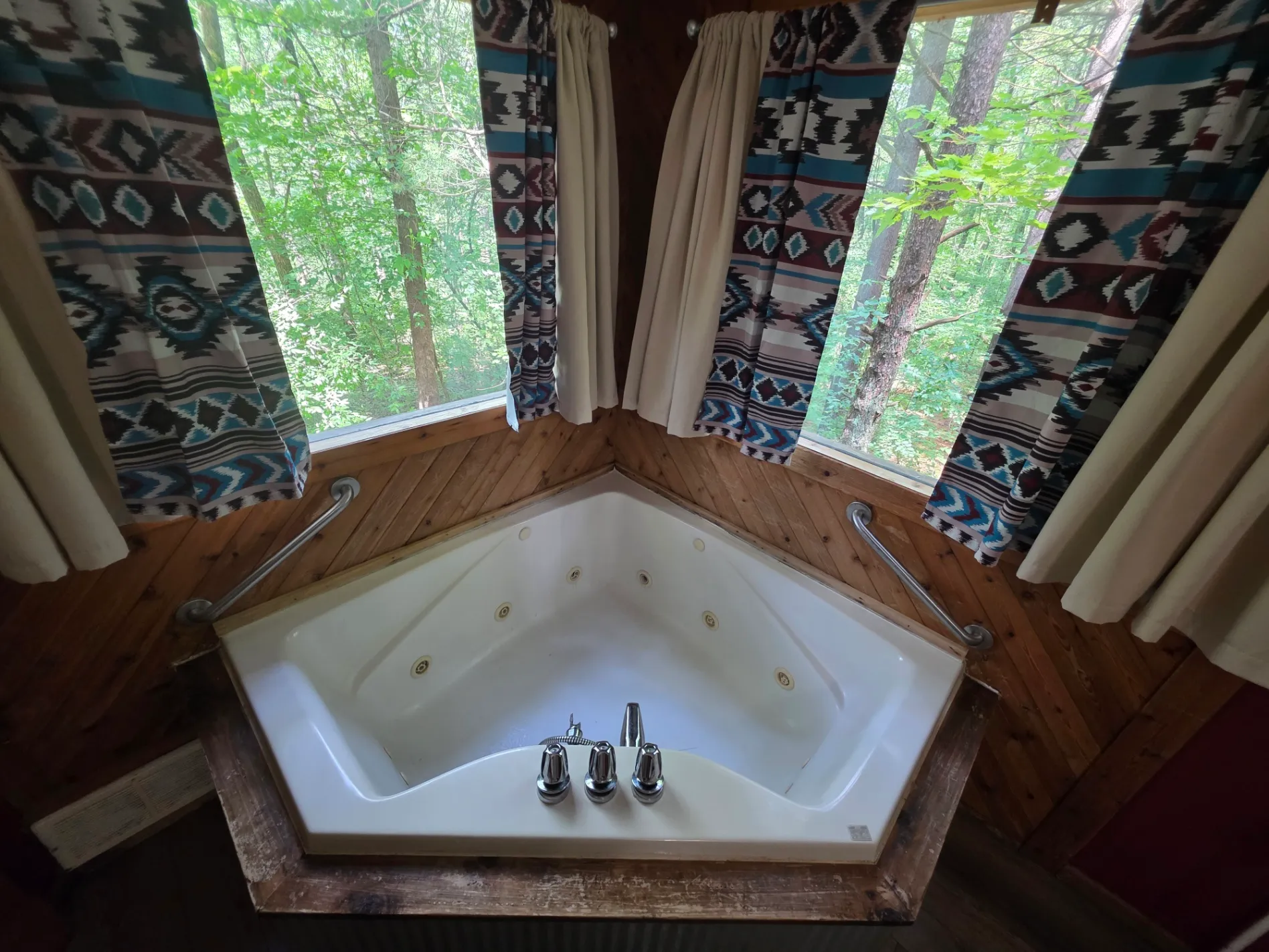 Corner jacuzzi tub with forest views through windows and Native American patterned curtains at Cherokee Way cabin