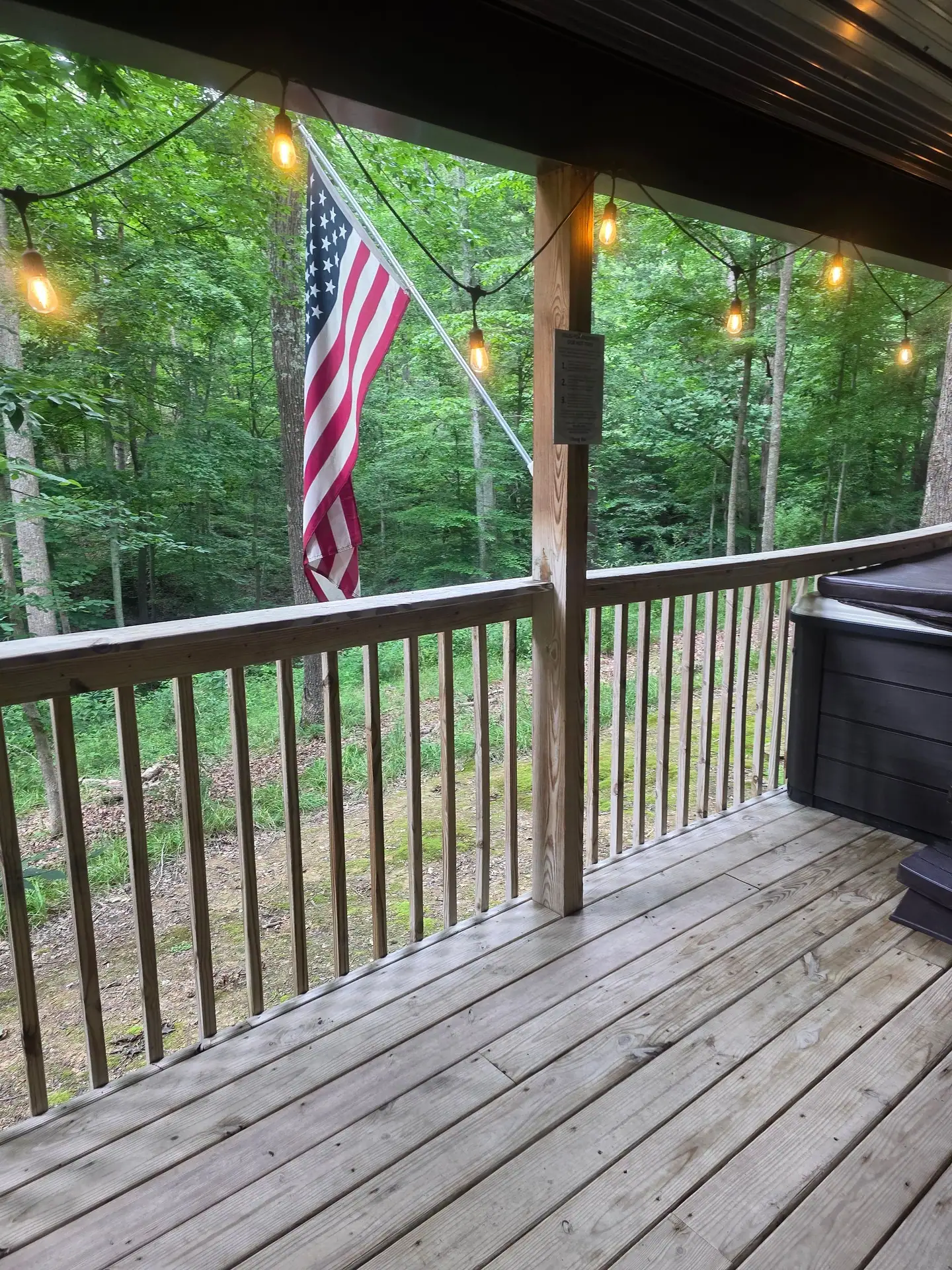 Covered deck with string lights, flag and forest view at Dogwood Run cabin