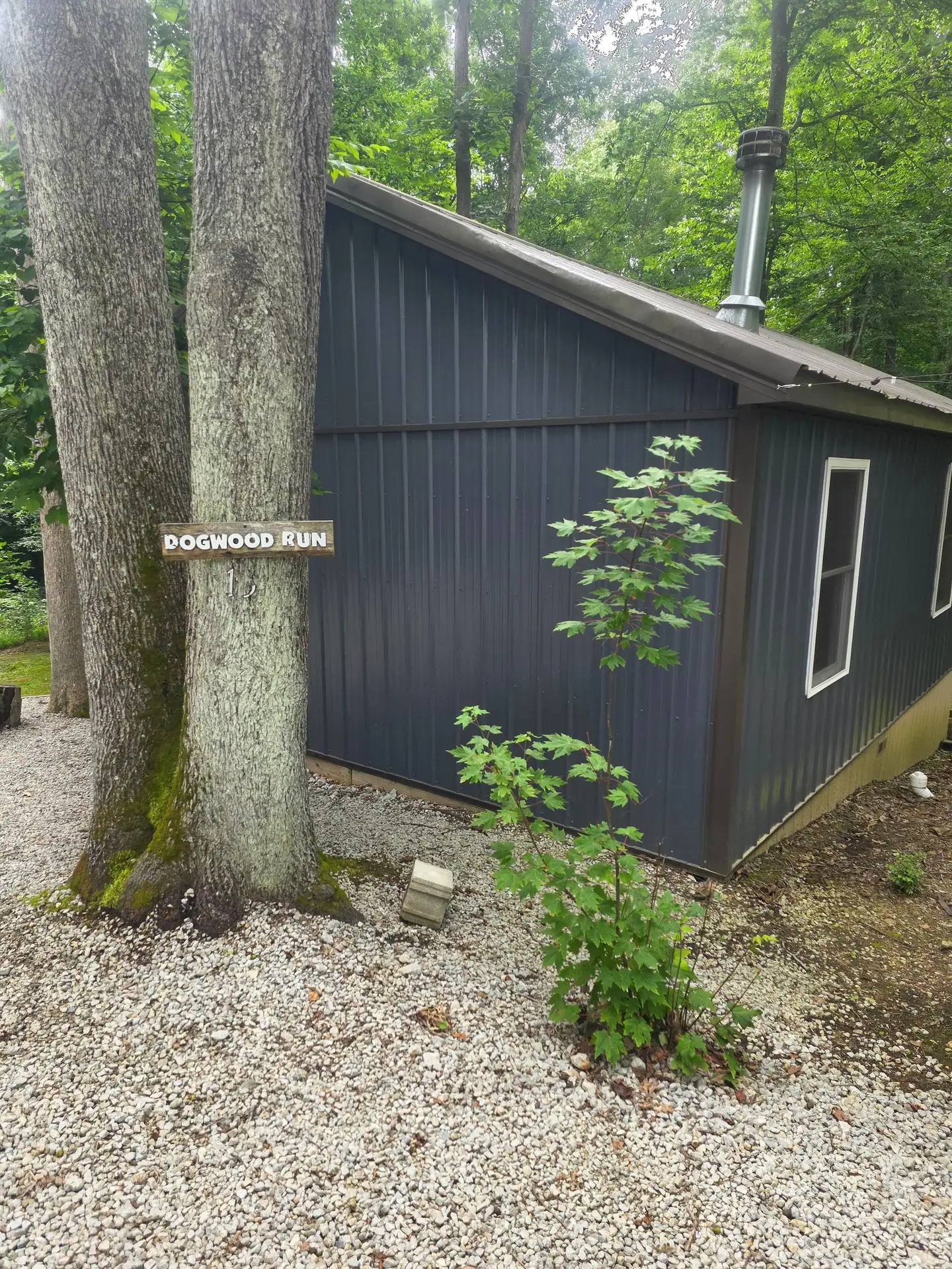 Side view of Dogwood Run cabin with the name sign on the tree and gravel yard