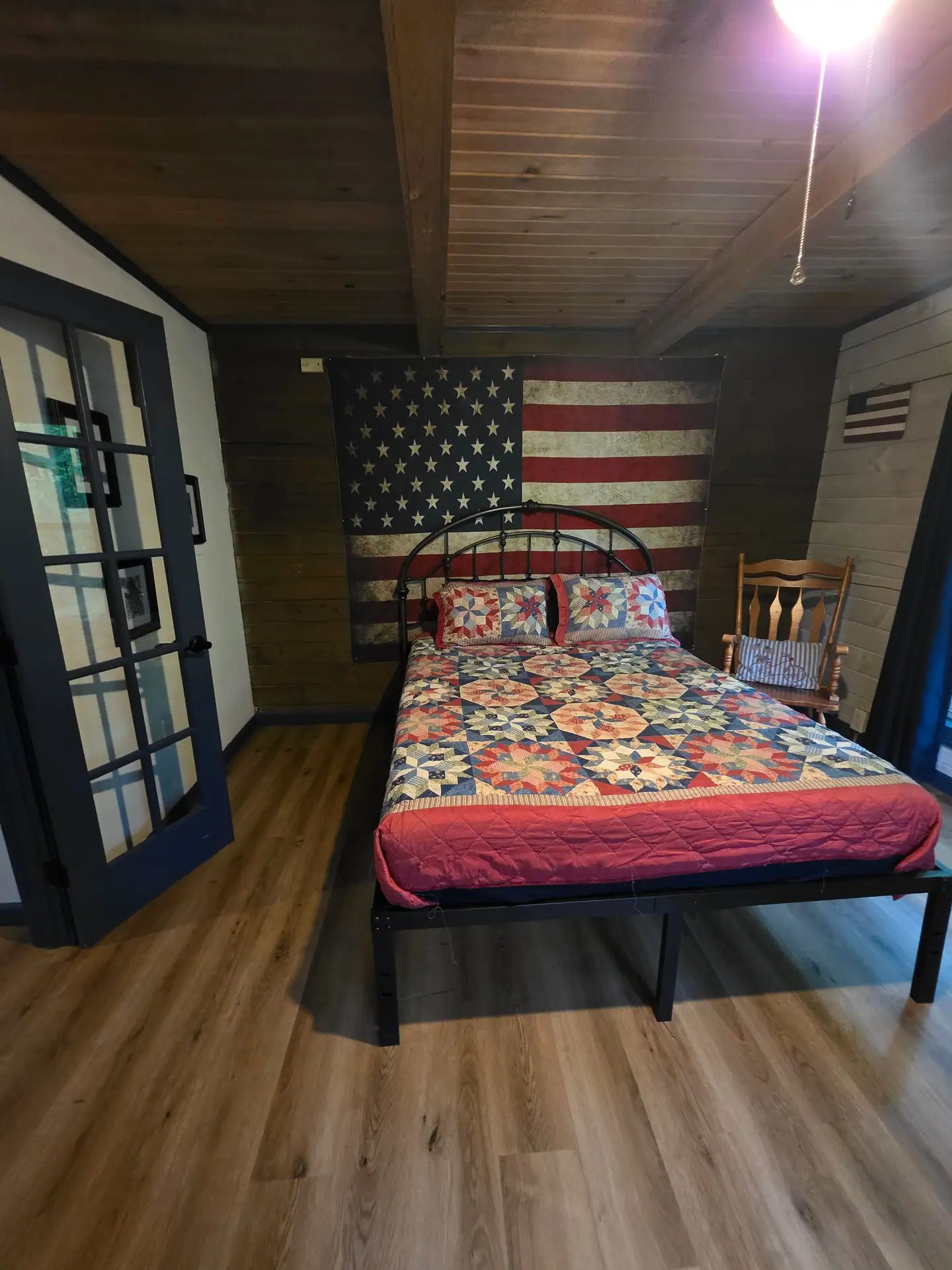 Eagles Nest cabin bedroom with iron bed, patriotic quilt and a large American flag on the wall