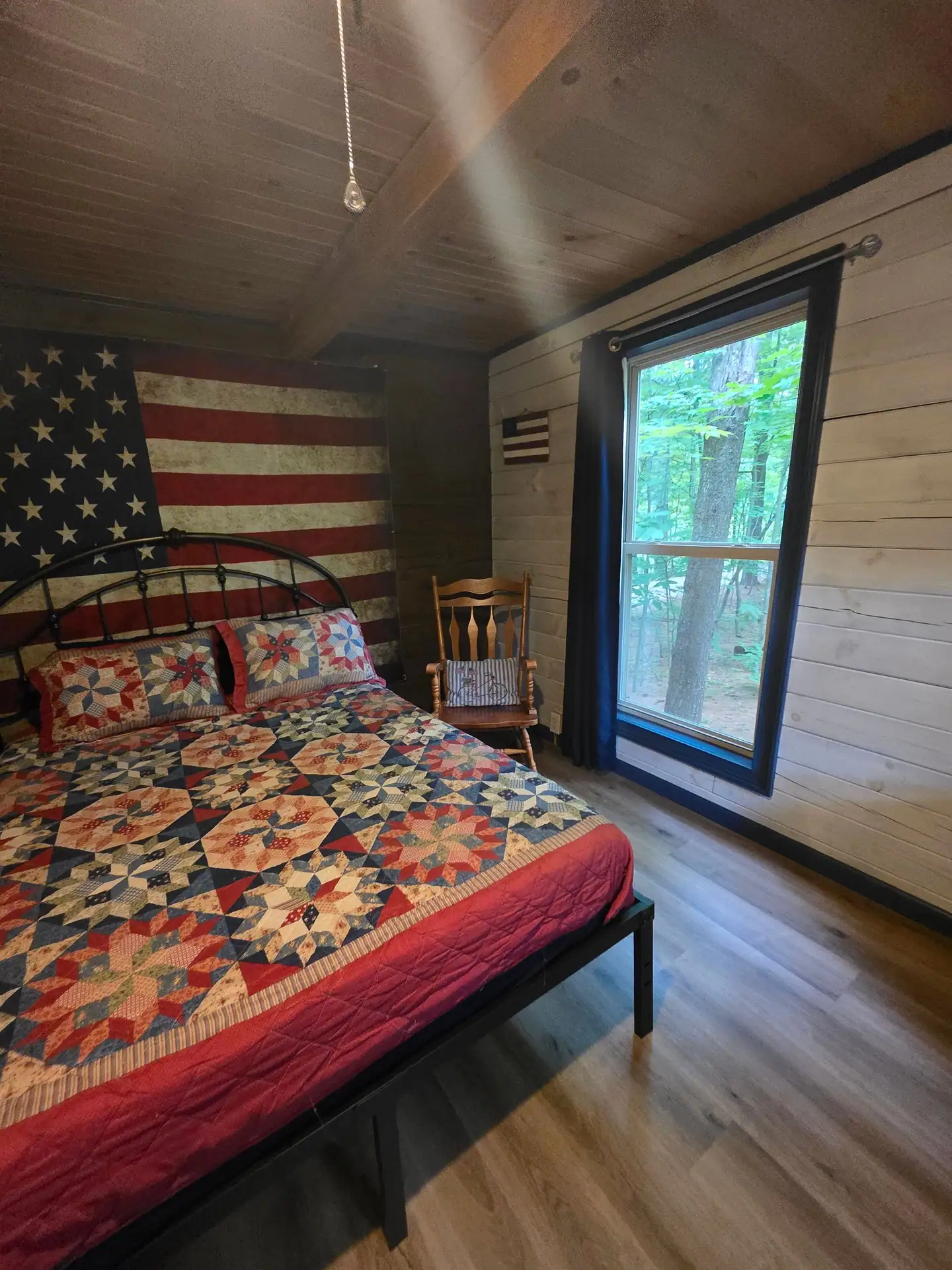 Eagles Nest cabin bedroom with patriotic quilt, rocking chair and a tall window to the woods