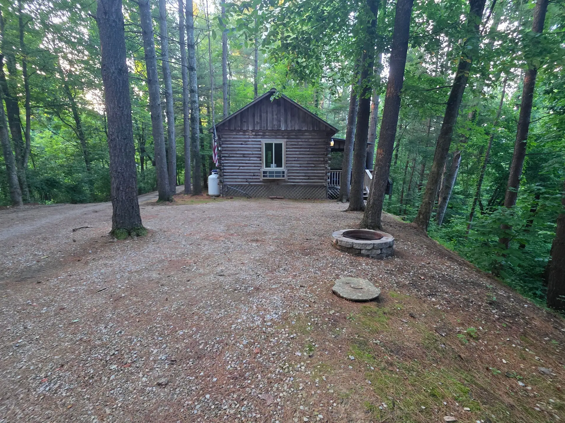 Eagles Nest log cabin seen across the gravel clearing with its stone fire pit