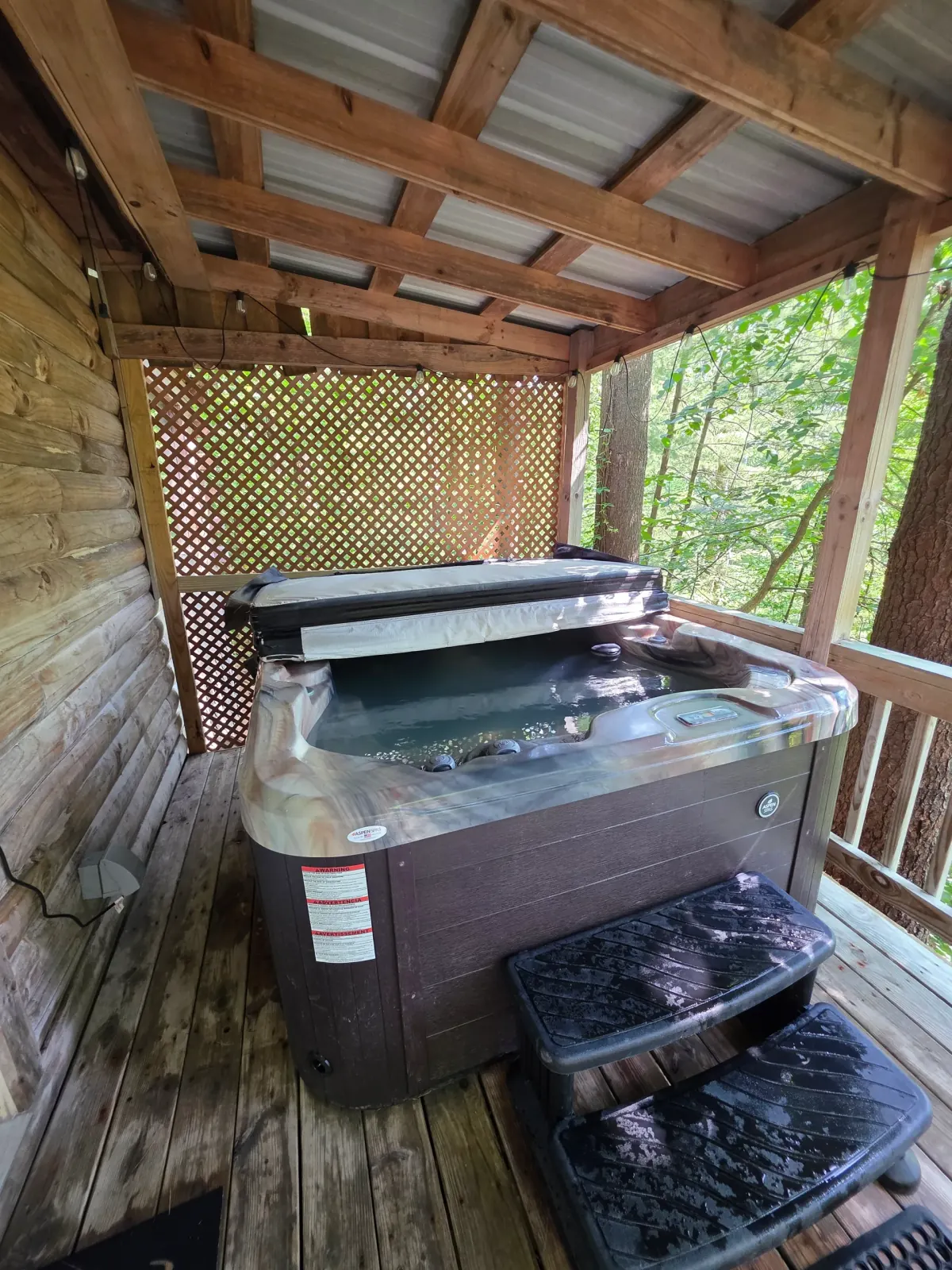 Private outdoor hot tub on covered wooden deck at Eagles Nest cabin surrounded by forest