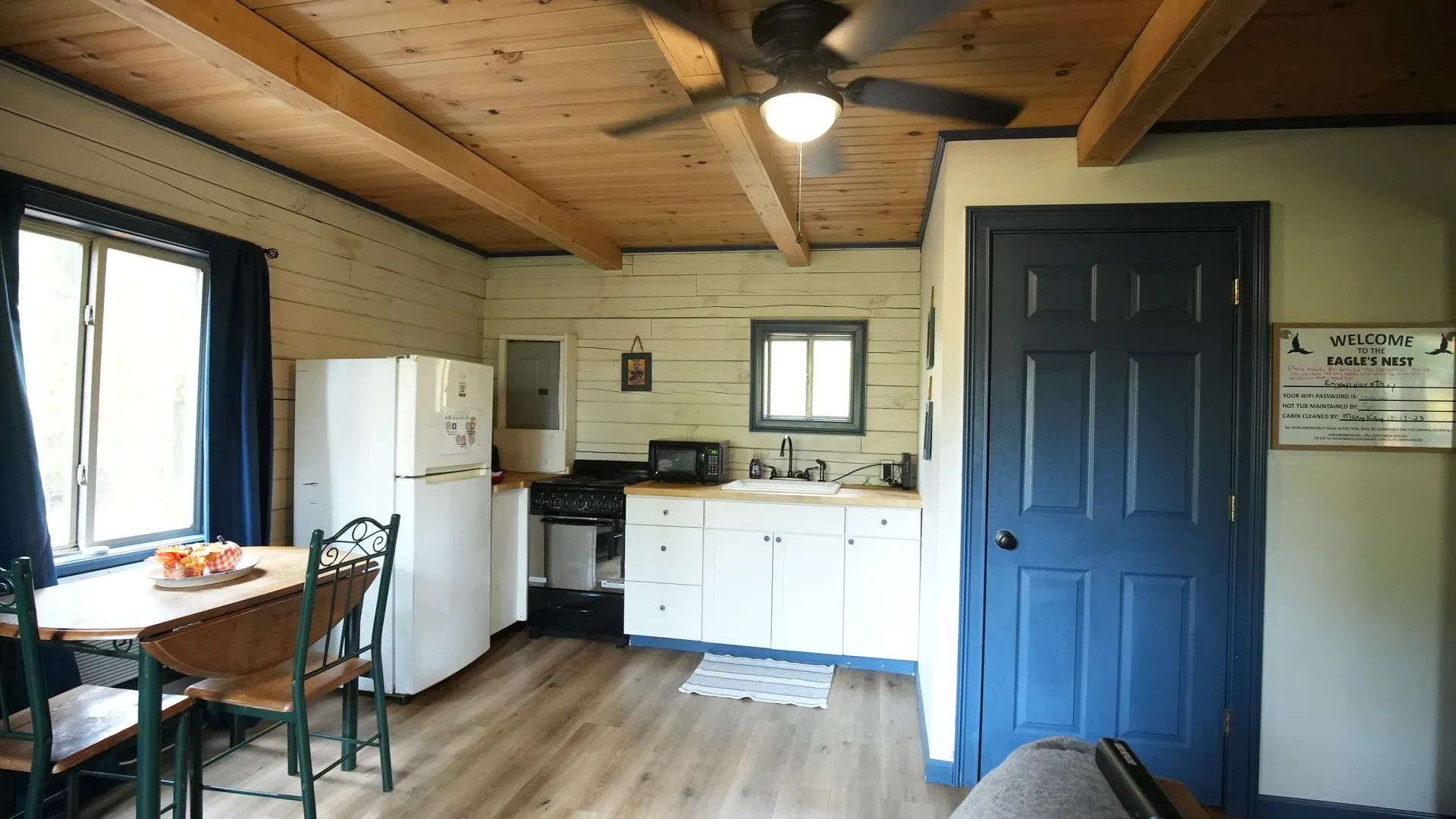 Eagles Nest cabin kitchen and dining area with welcome sign, white cabinets, and wood beam ceiling