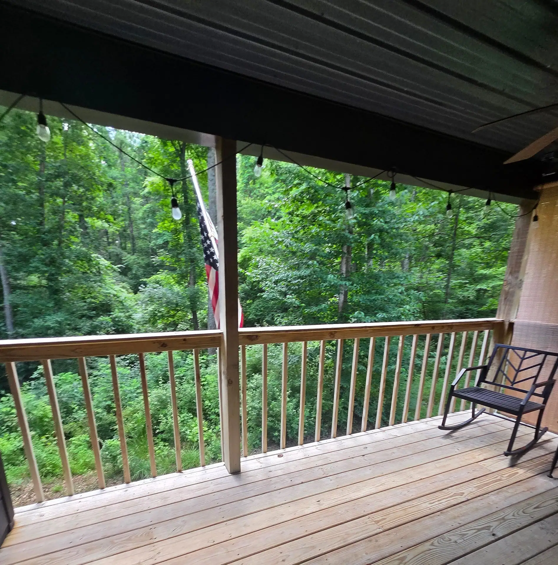 Covered back deck with a rocking chair and a view into the woods at Firefly's Landing