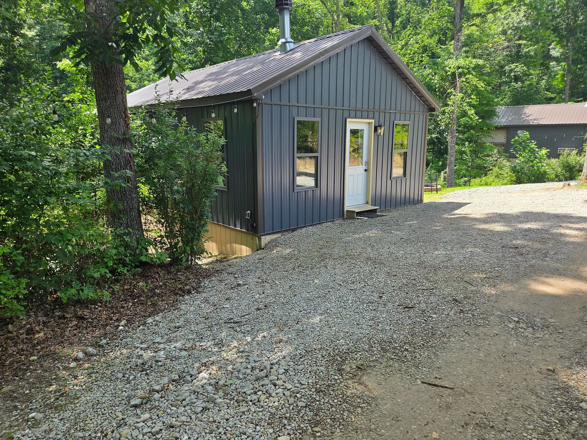 Front entry of Firefly's Landing cabin with dark gray metal siding beside the gravel drive