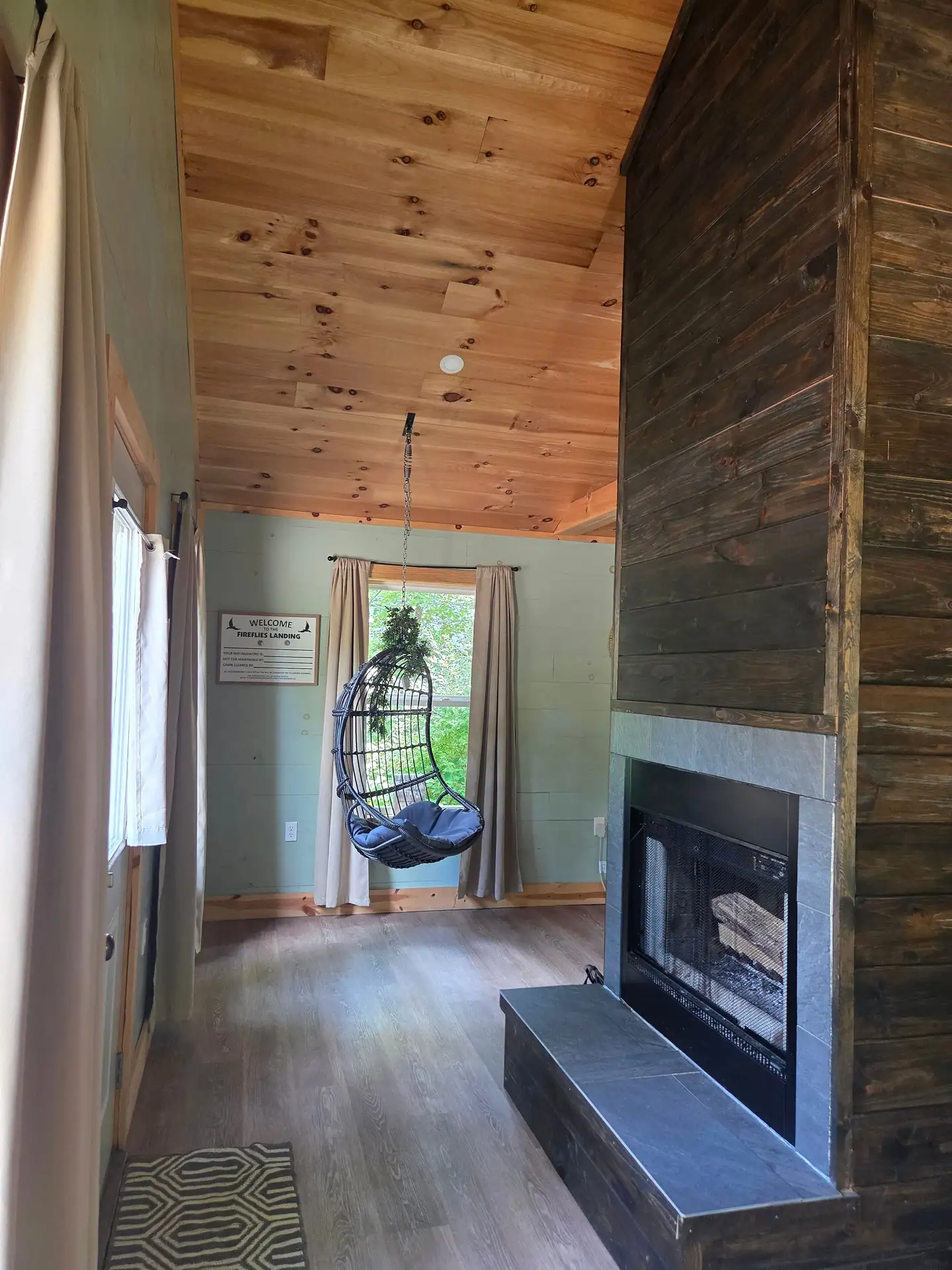 Double-sided wood-burning fireplace with the hanging egg chair beyond at Firefly's Landing