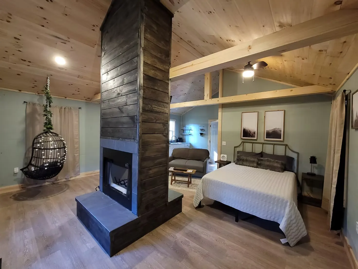 Open-concept living room with double-sided cedar fireplace and hanging egg chair at Firefly cabin