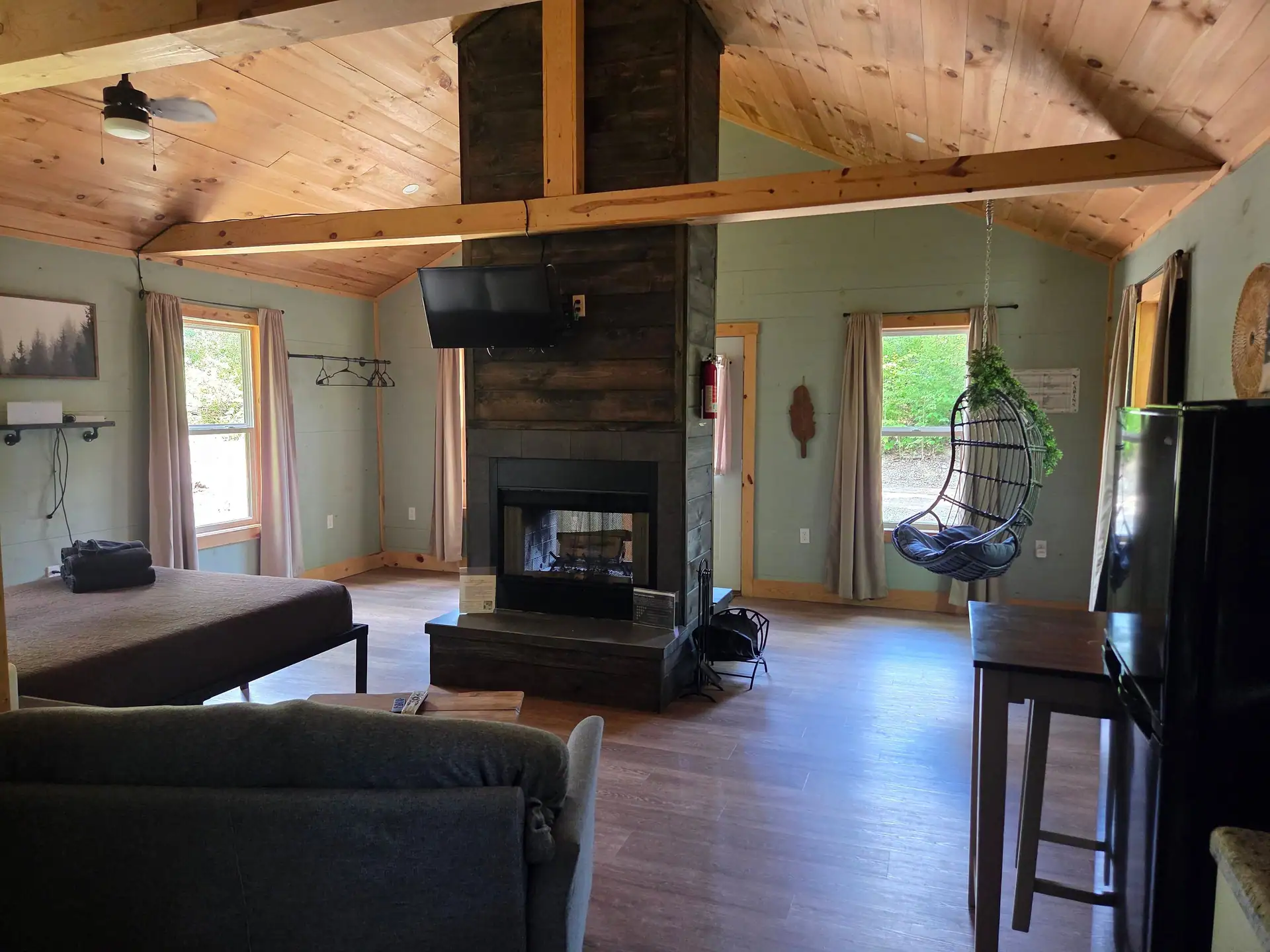 Open-plan interior with double-sided fireplace, queen bed and hanging egg chair at Firefly's Landing