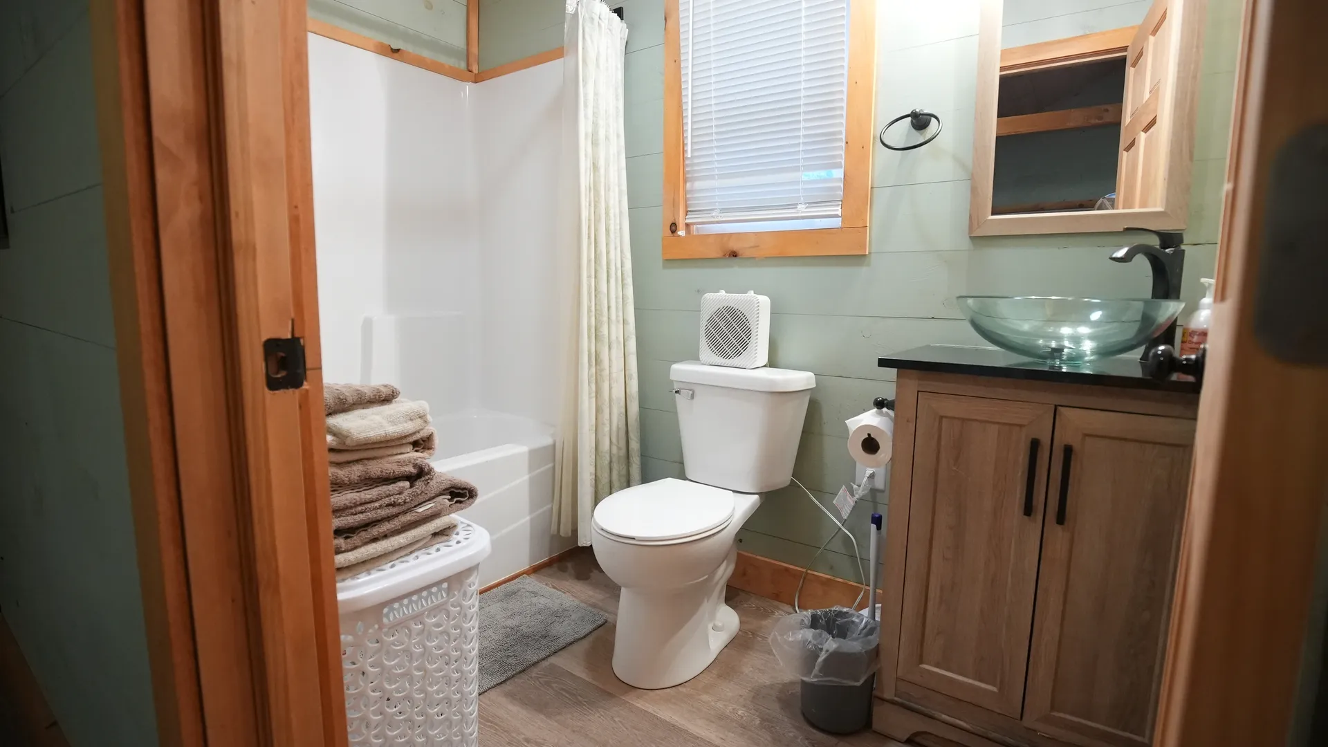 Bathroom with tub-shower combo, glass vessel sink vanity, and green accent wall at Forest Aisle cabin