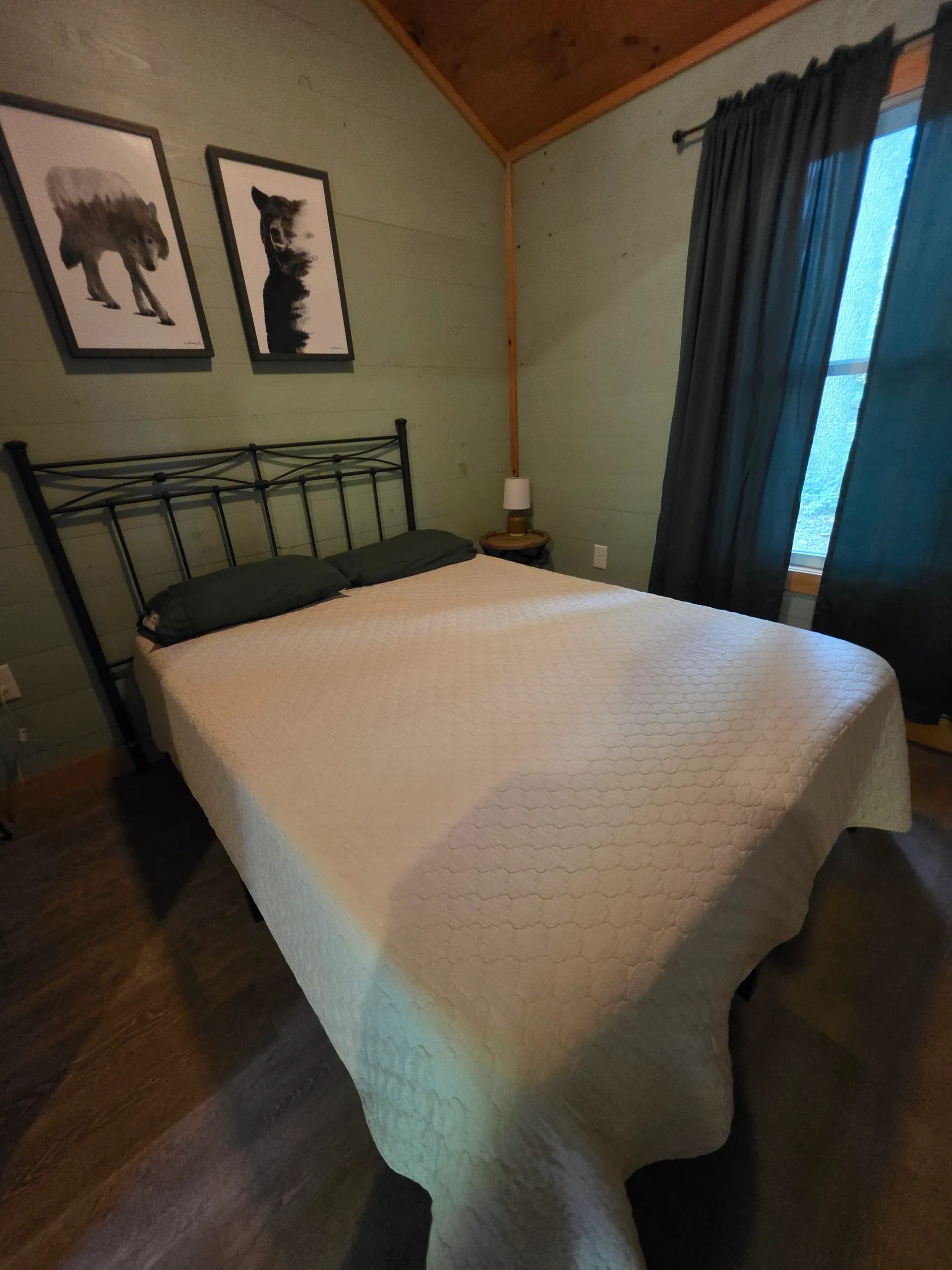 Queen bed with white quilt and bear artwork on green wall at Forest Aisle cabin