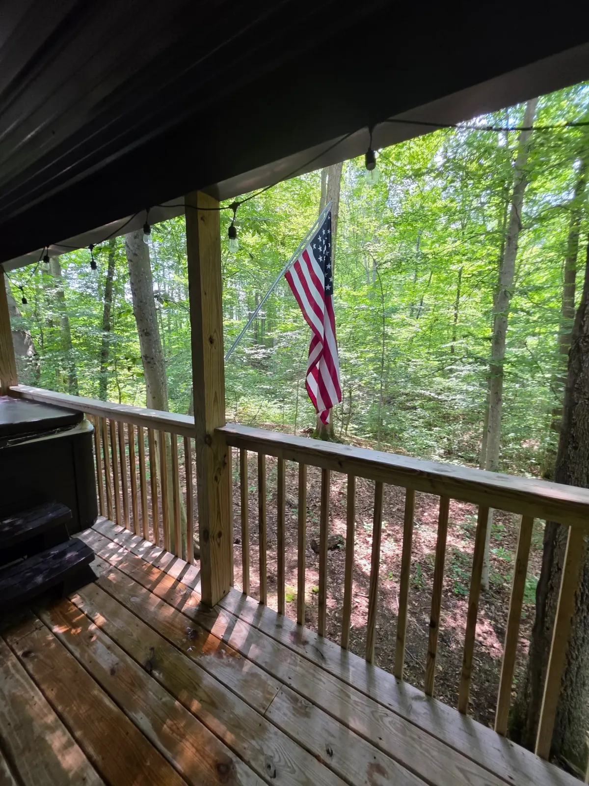 Deck with American flag and pergola looking out into the summer forest at Forest Aisle cabin
