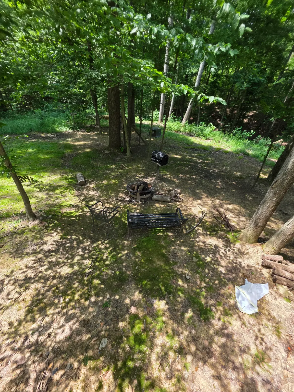 Fire pit with bench seating and charcoal grill in the wooded yard at Forest Aisle cabin