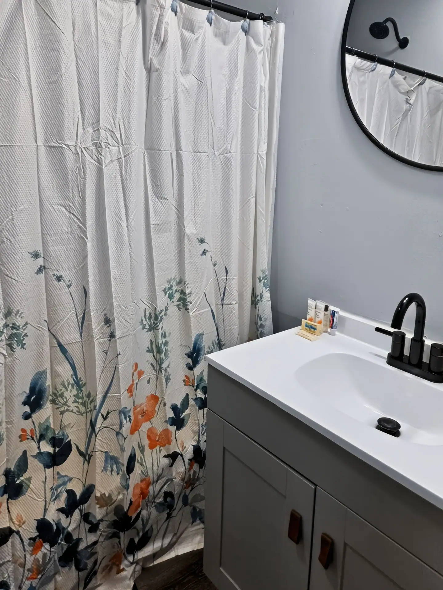First bathroom at The Getaway House with a vanity, round mirror and floral shower curtain.