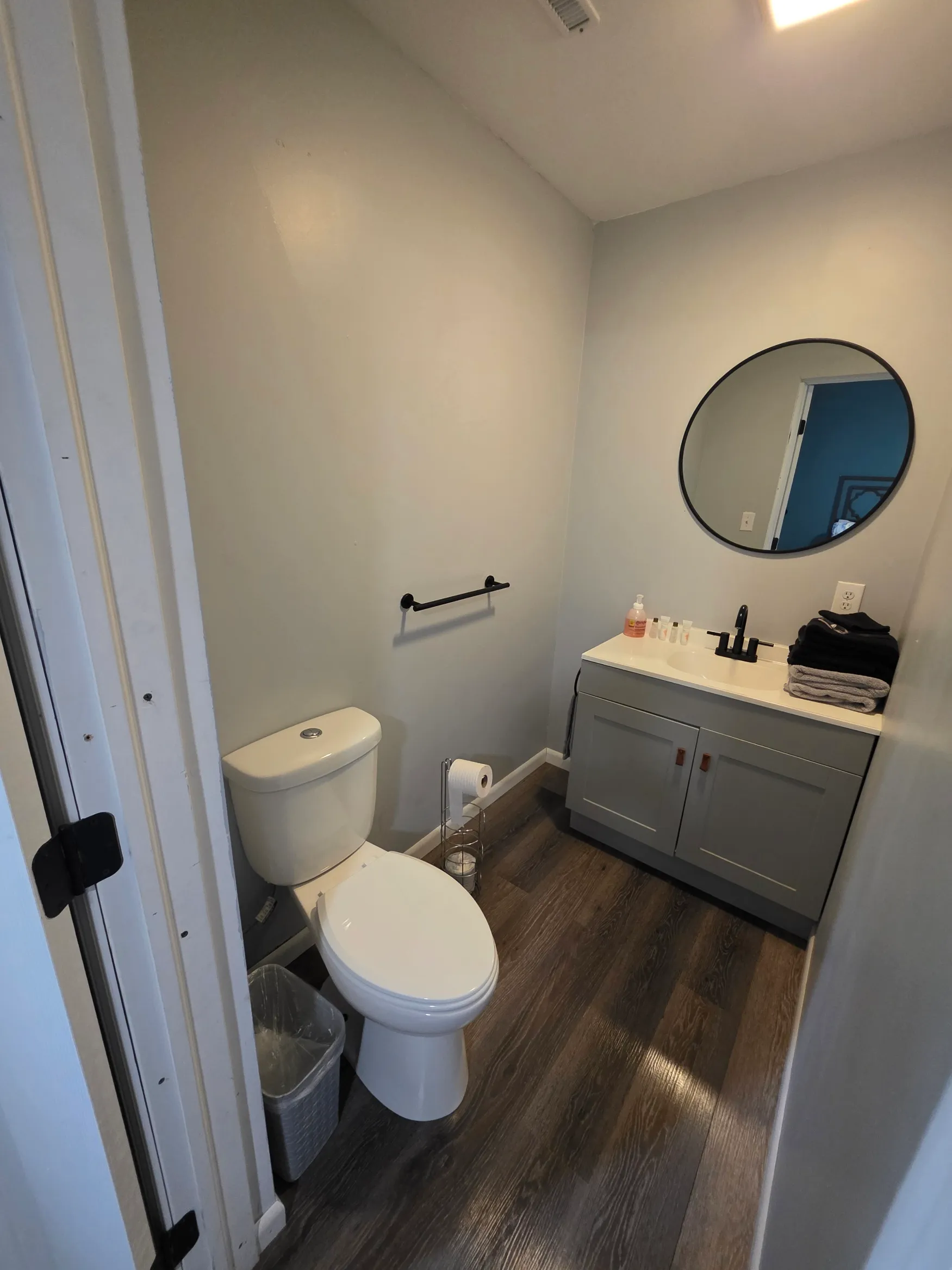 Modern bathroom with round mirror, gray vanity, and hardwood floors at Getaway House cabin