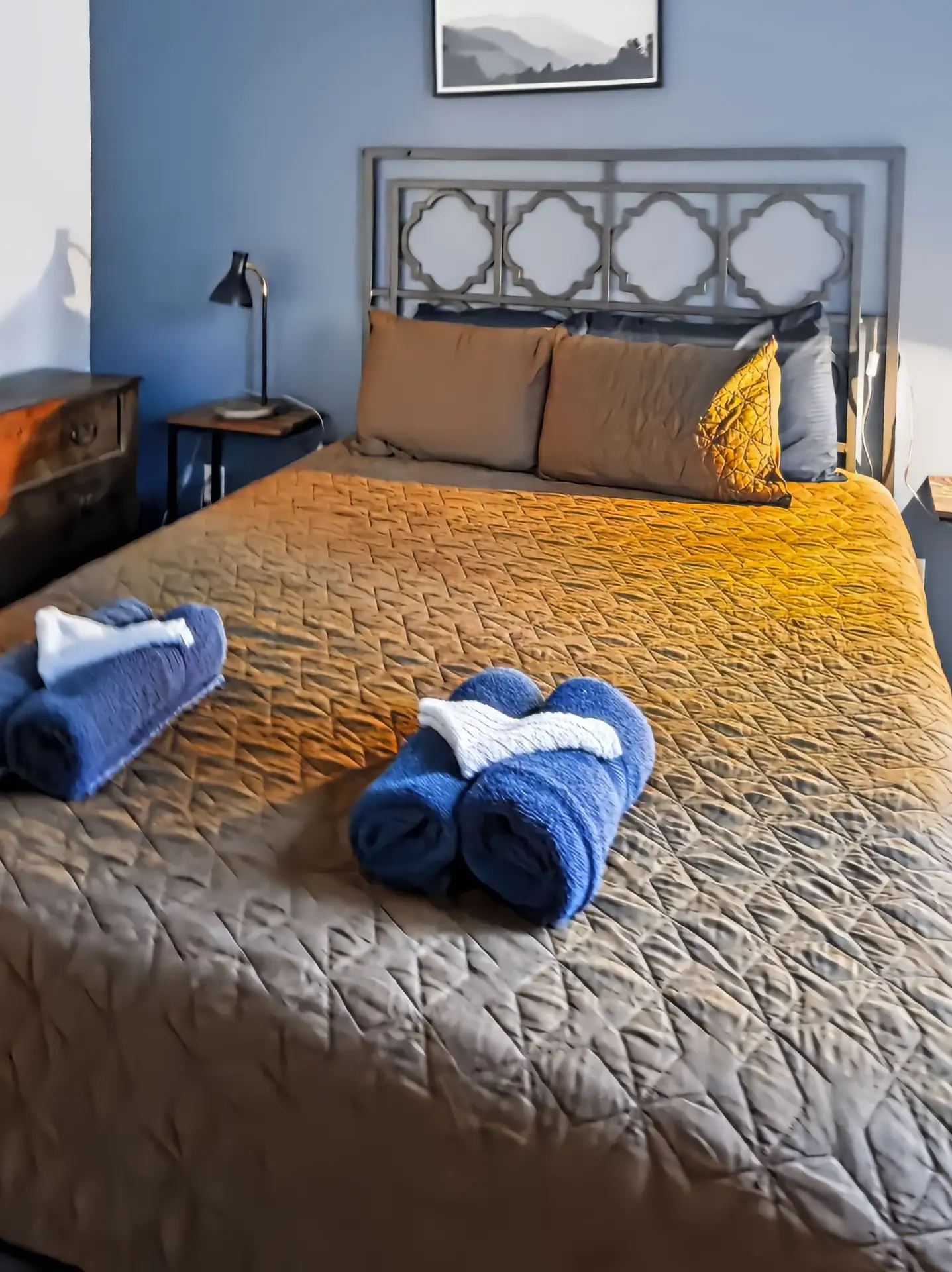 Queen bed with a metal headboard and fresh towels in the second bedroom of The Getaway House.