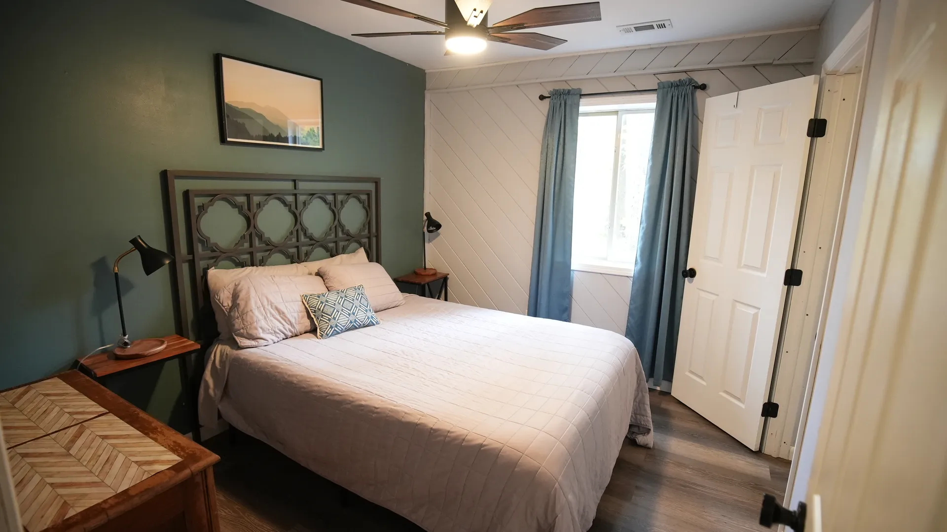 Bedroom with queen bed, geometric metal headboard, green accent wall, and reading lamps at Getaway House cabin