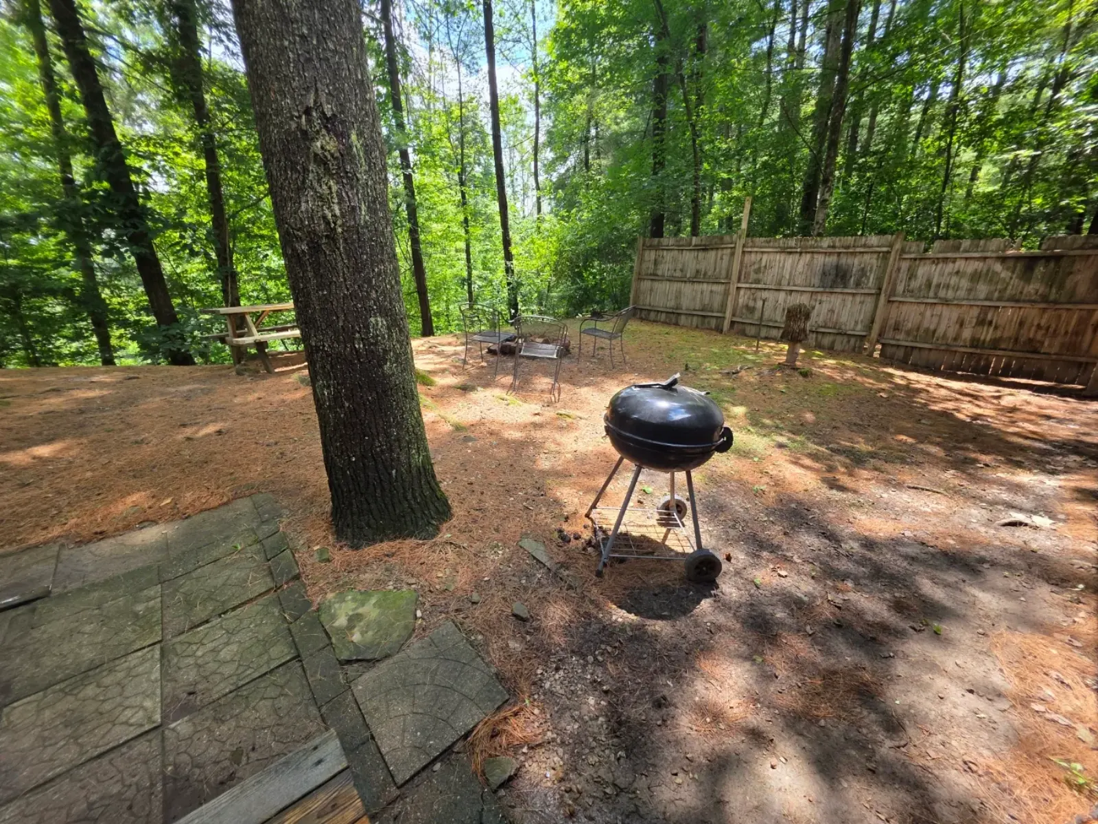 Charcoal grill, picnic table, and fenced backyard with fire pit among the trees at Getaway House cabin