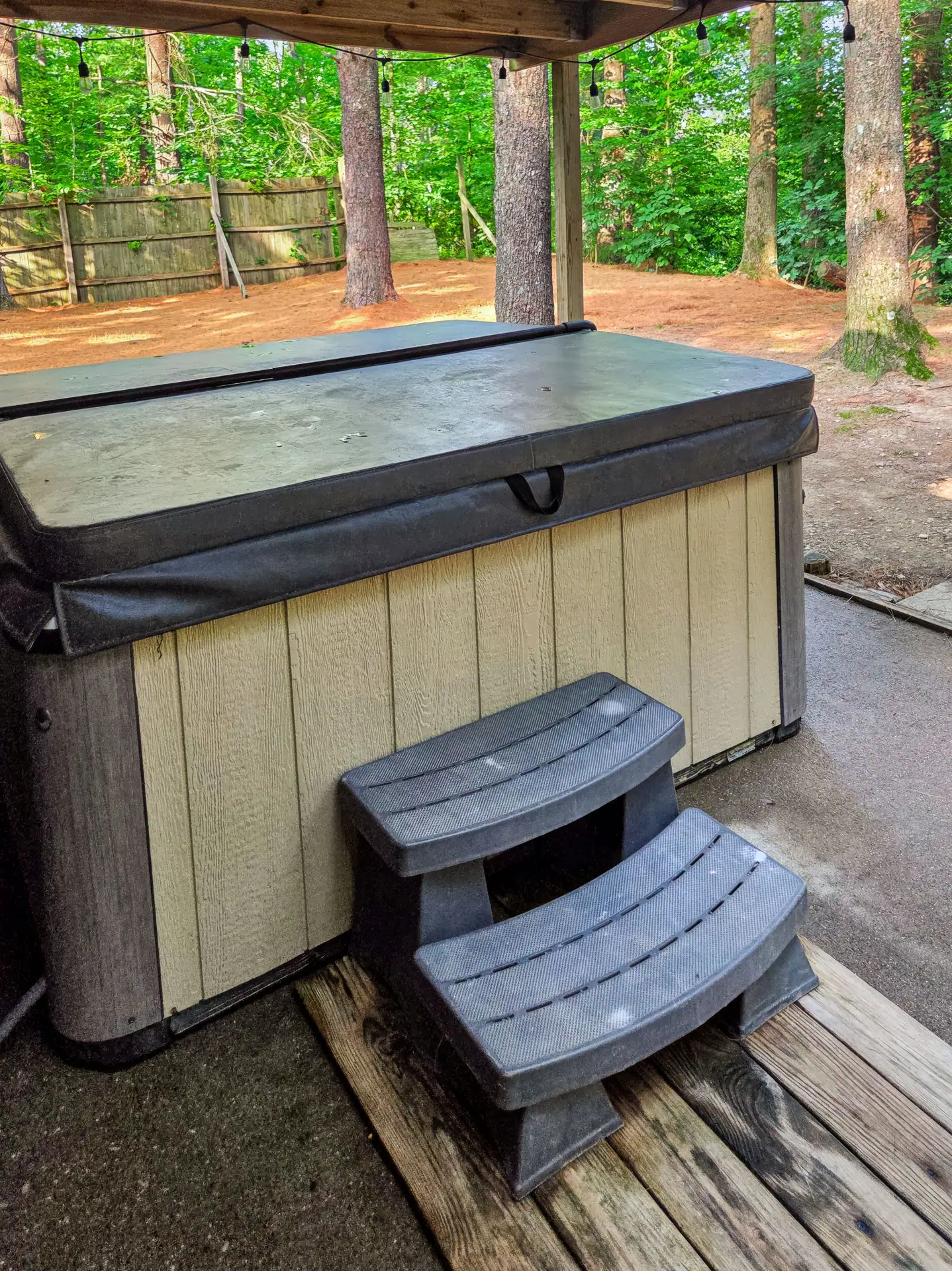 Private covered hot tub with steps at The Getaway House, with the fenced yard behind.