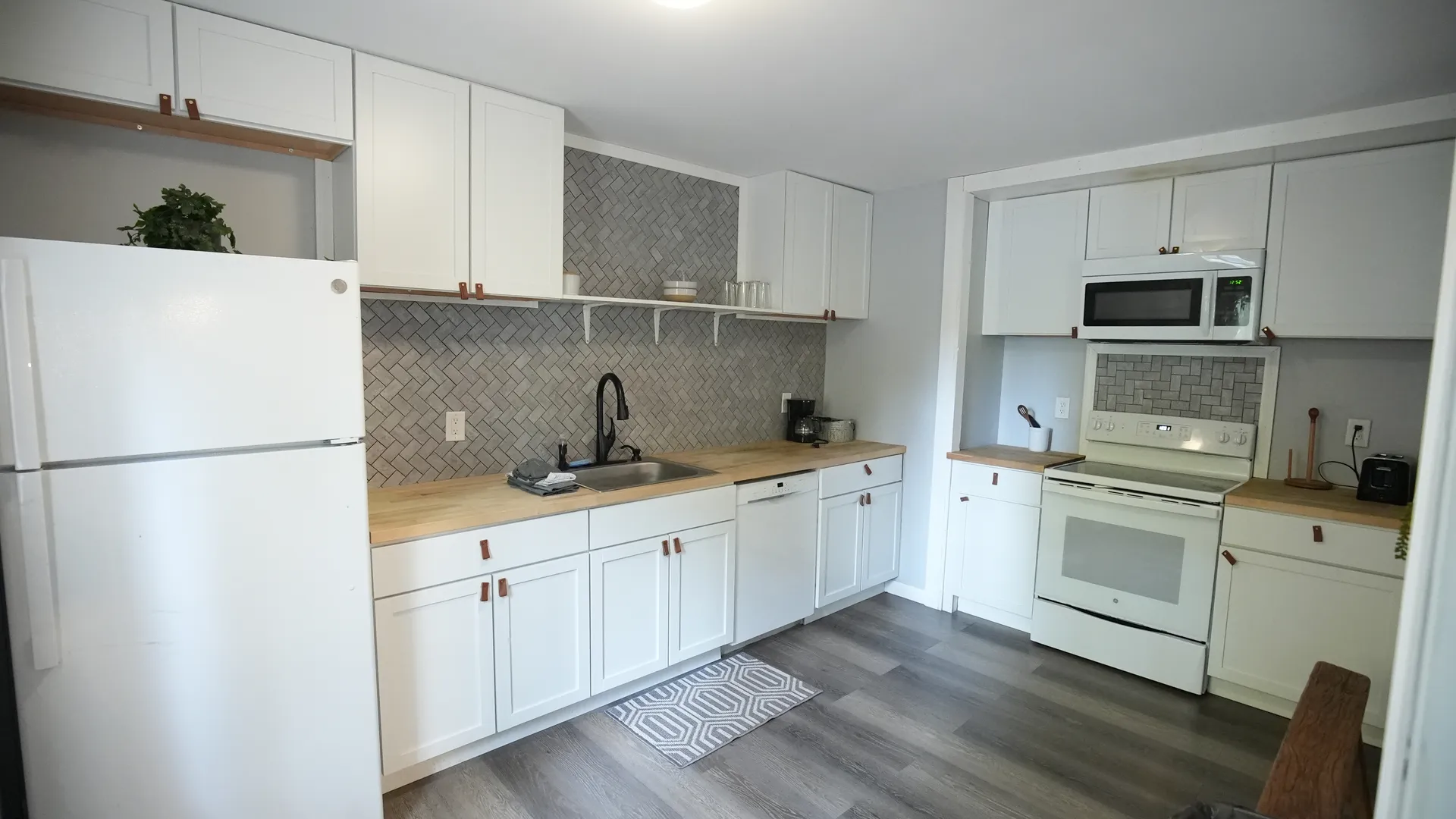 Full kitchen with white cabinets, herringbone tile backsplash, stove, microwave, and butcher block counters at Getaway House cabin