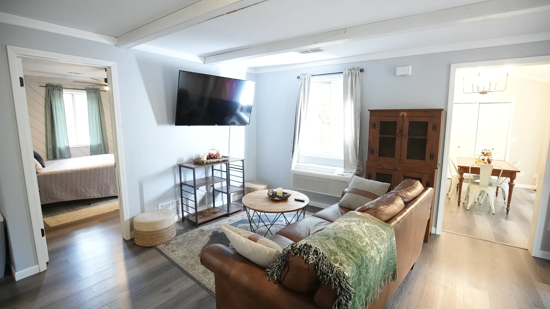 Wide view of living room with leather sofa, wall-mounted TV, area rug, and views to bedroom and dining room at Getaway House cabin