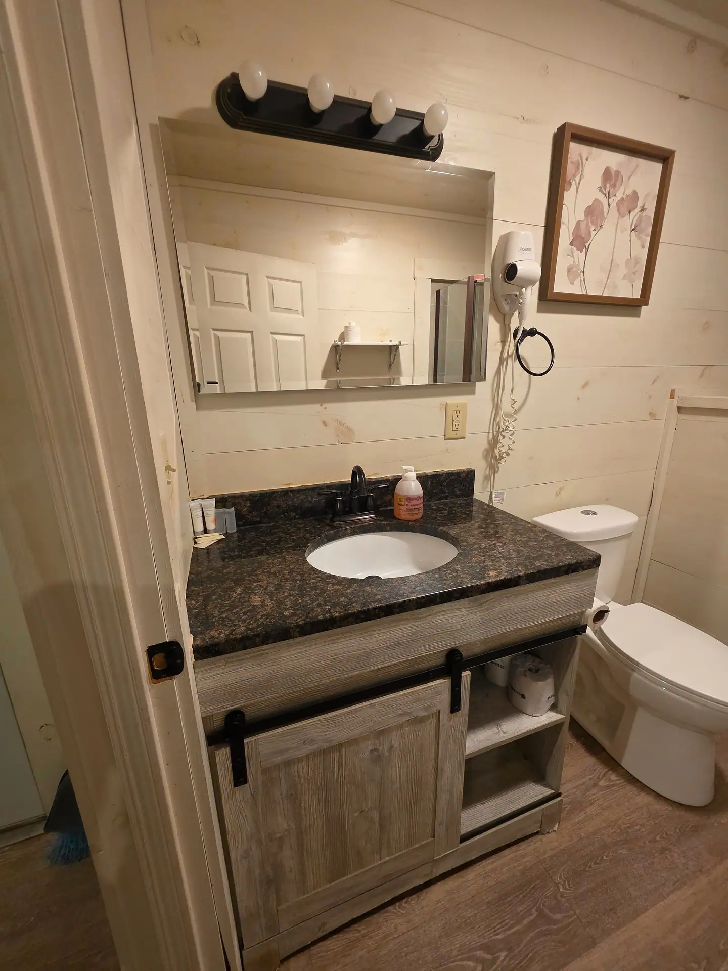 Bathroom vanity with dark granite top, sliding barn door cabinet, mirror and hair dryer at Hummingbird cabin
