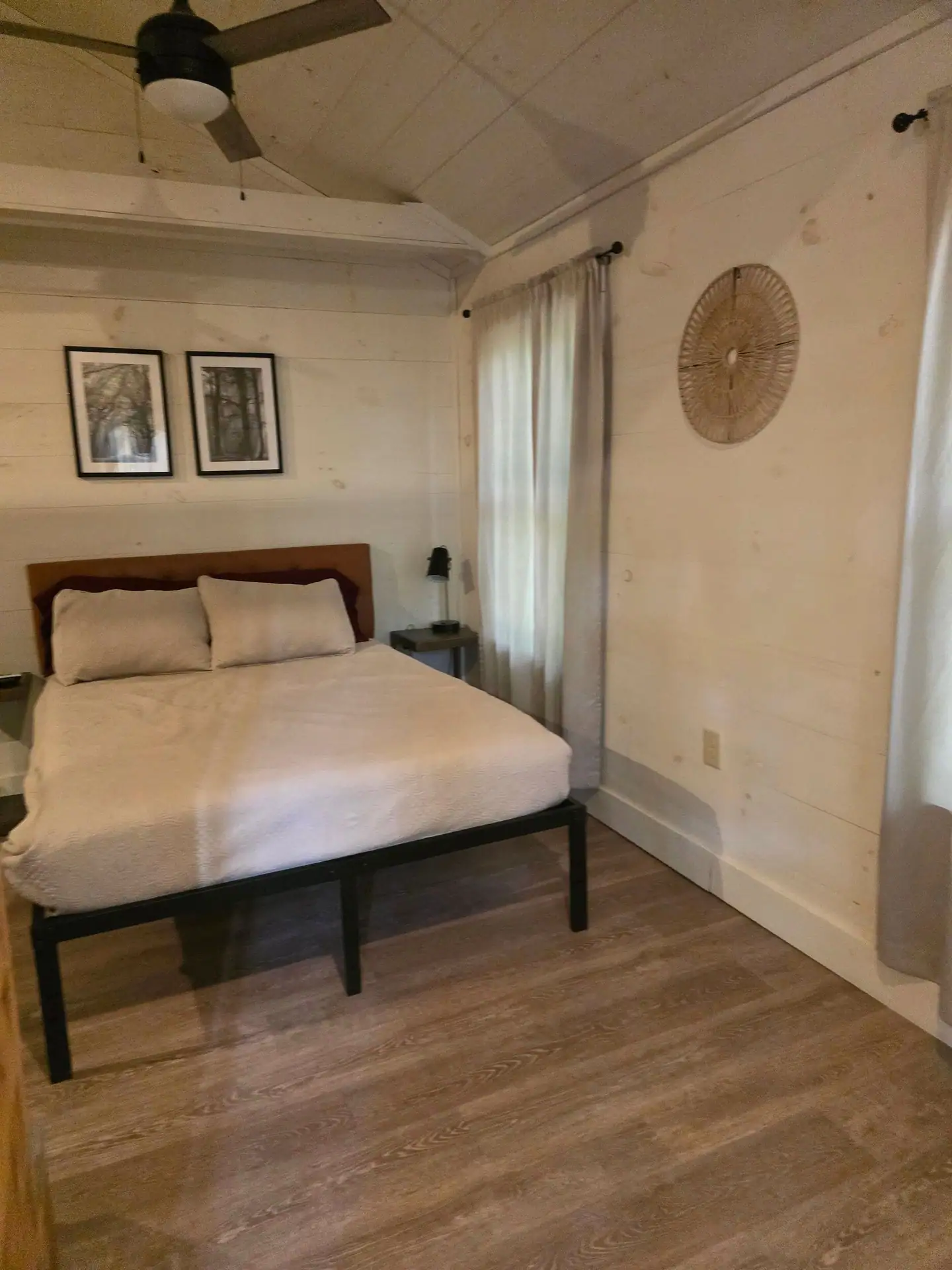 Queen bed with cream bedding, wooden headboard and framed black-and-white prints at Hummingbird cabin