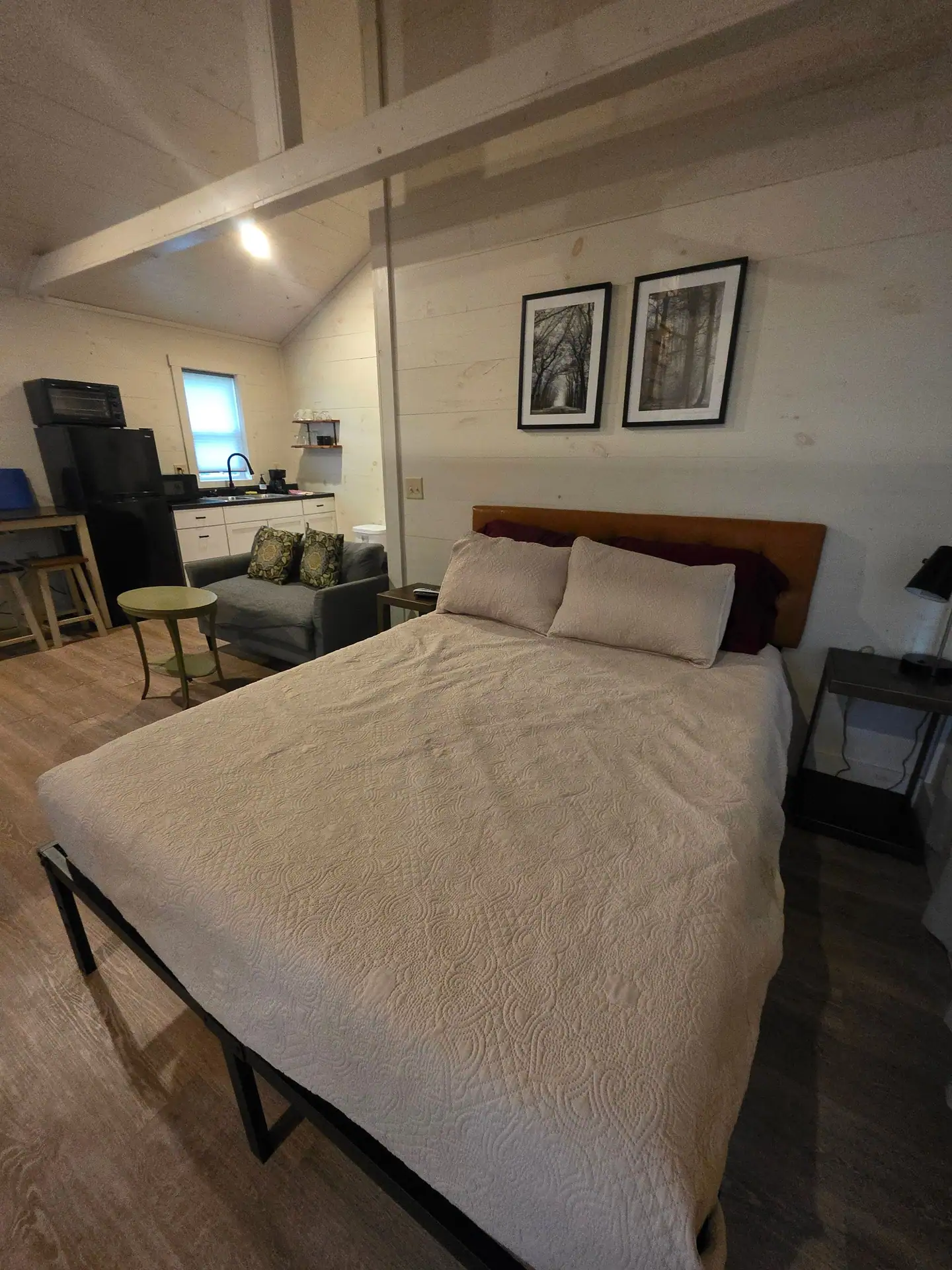 Queen bed with cream quilt and the kitchenette and sofa in the background at Hummingbird cabin