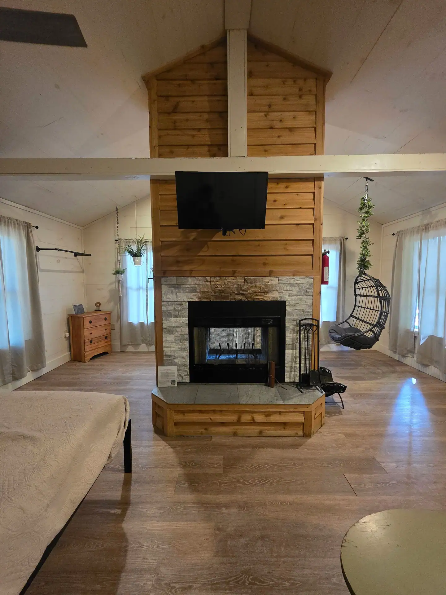 Double-sided wood-burning fireplace with cedar and stone surround, mounted TV and hanging egg chair at Hummingbird cabin