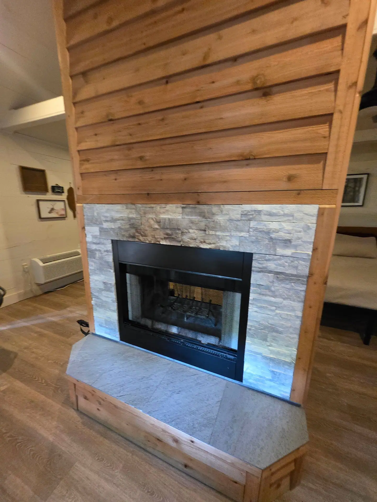 Wood-burning fireplace with stacked stone, cedar chimney and tiled hearth seen from the living area at Hummingbird cabin