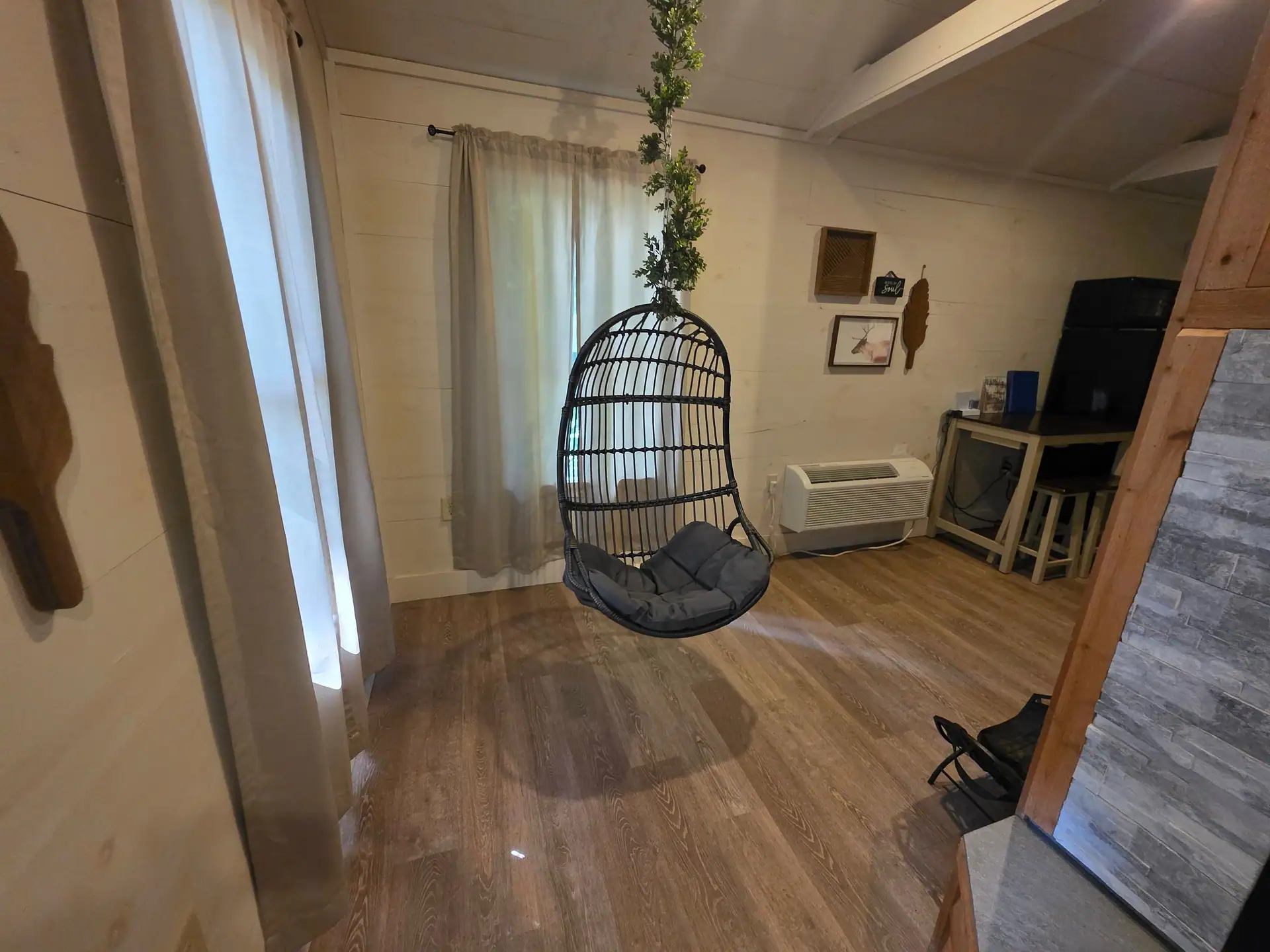 Hanging egg chair with gray cushion beside a curtained window at Hummingbird cabin