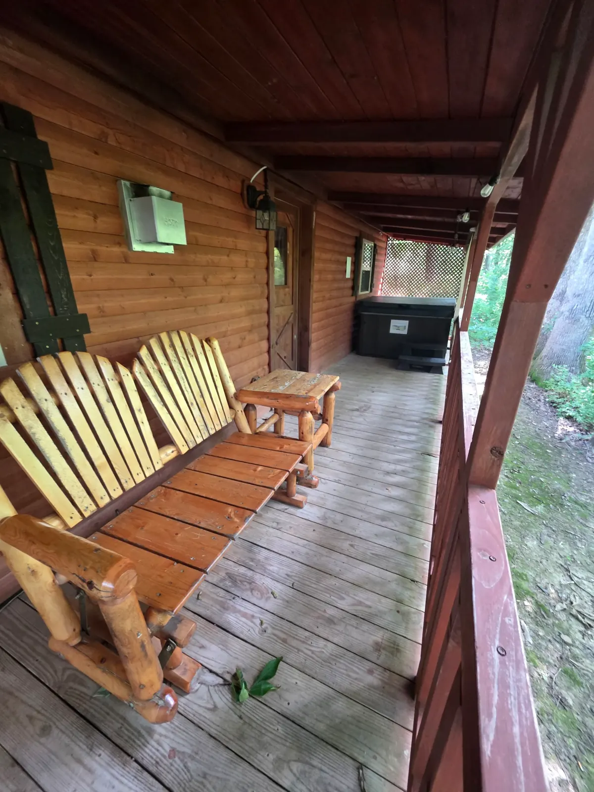 Covered back deck with rustic log bench and hot tub at Millers Den cabin