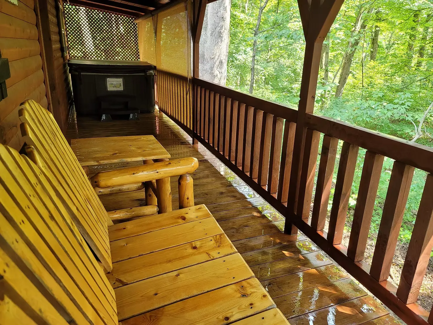 Covered deck with log bench seating and hot tub surrounded by forest at Millers Den cabin