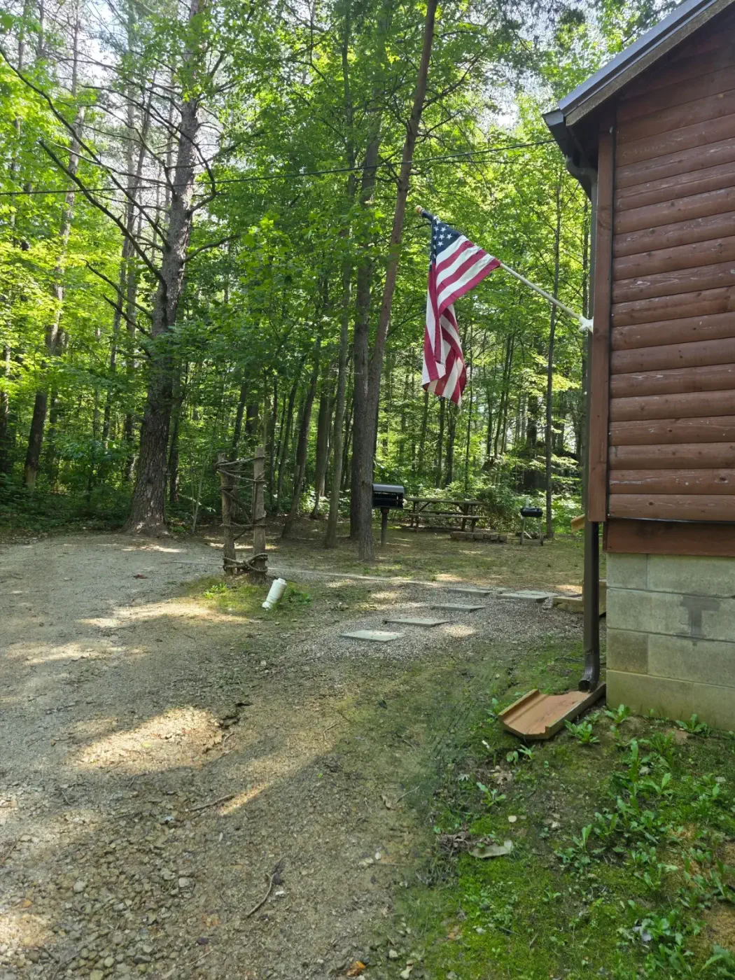 Driveway approach to Millers Den cabin with American flag and shaded forest lot